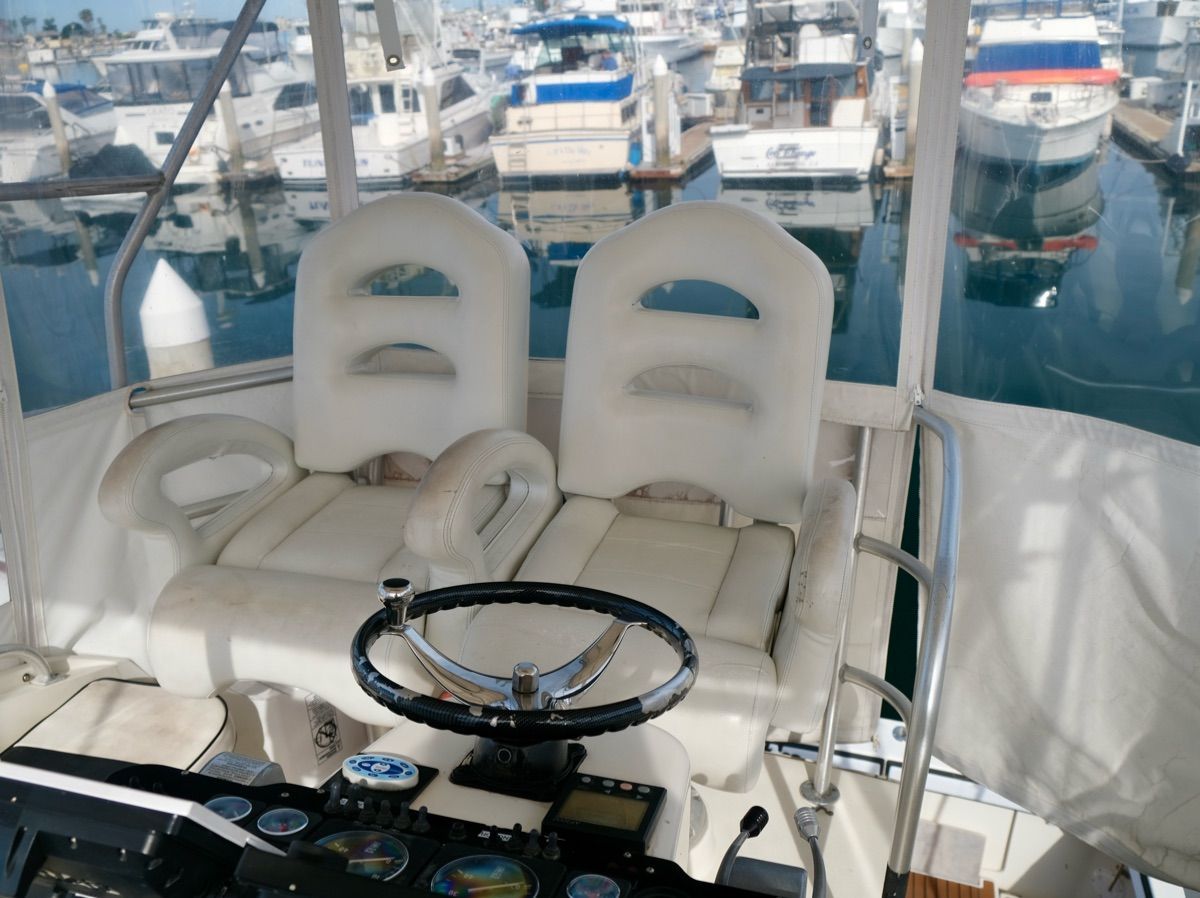 Two white seats on a boat overlooking a marina filled with boats.