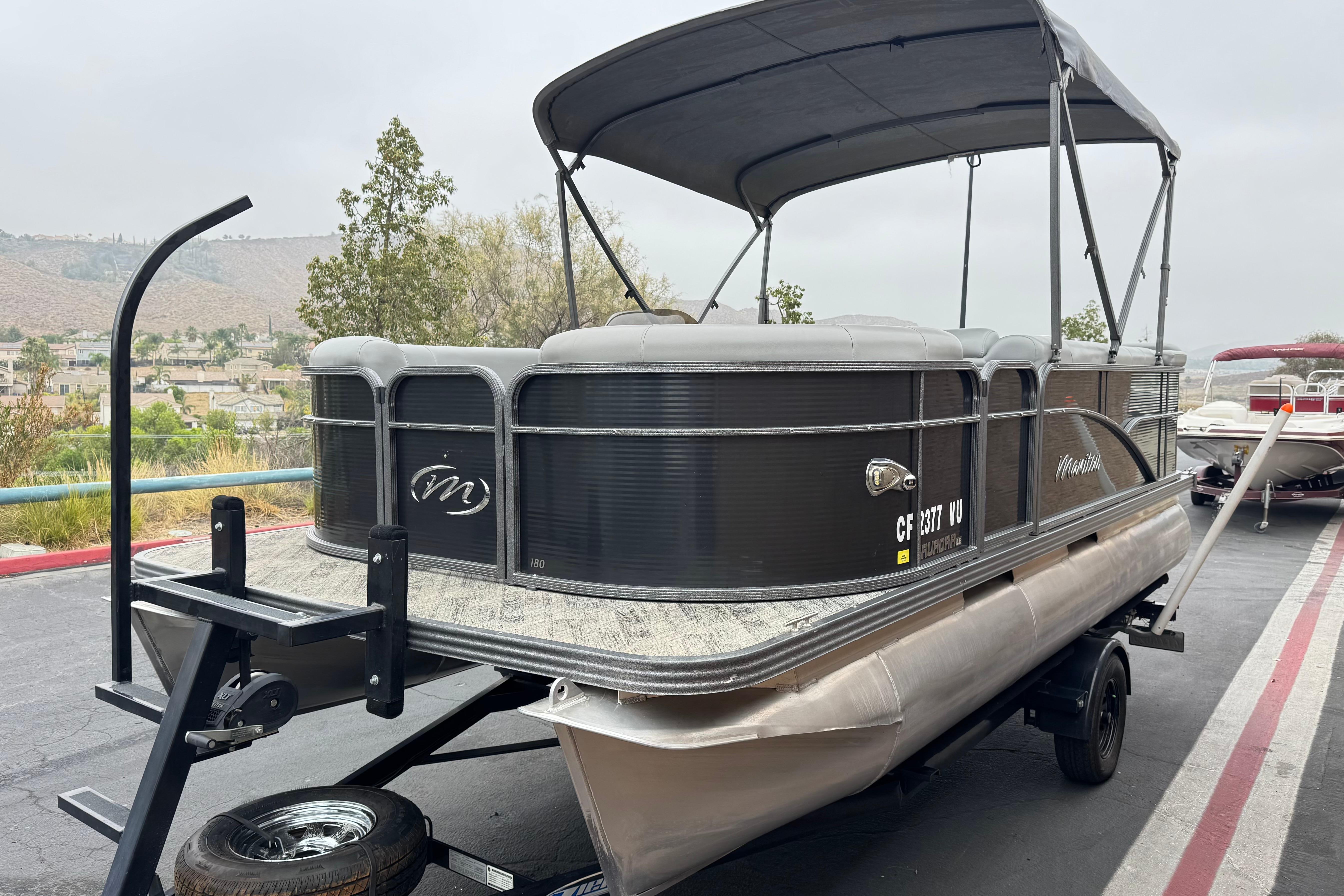 2020 Manitou 18 Aurora LE pontoon boat on trailer, parked outdoors.