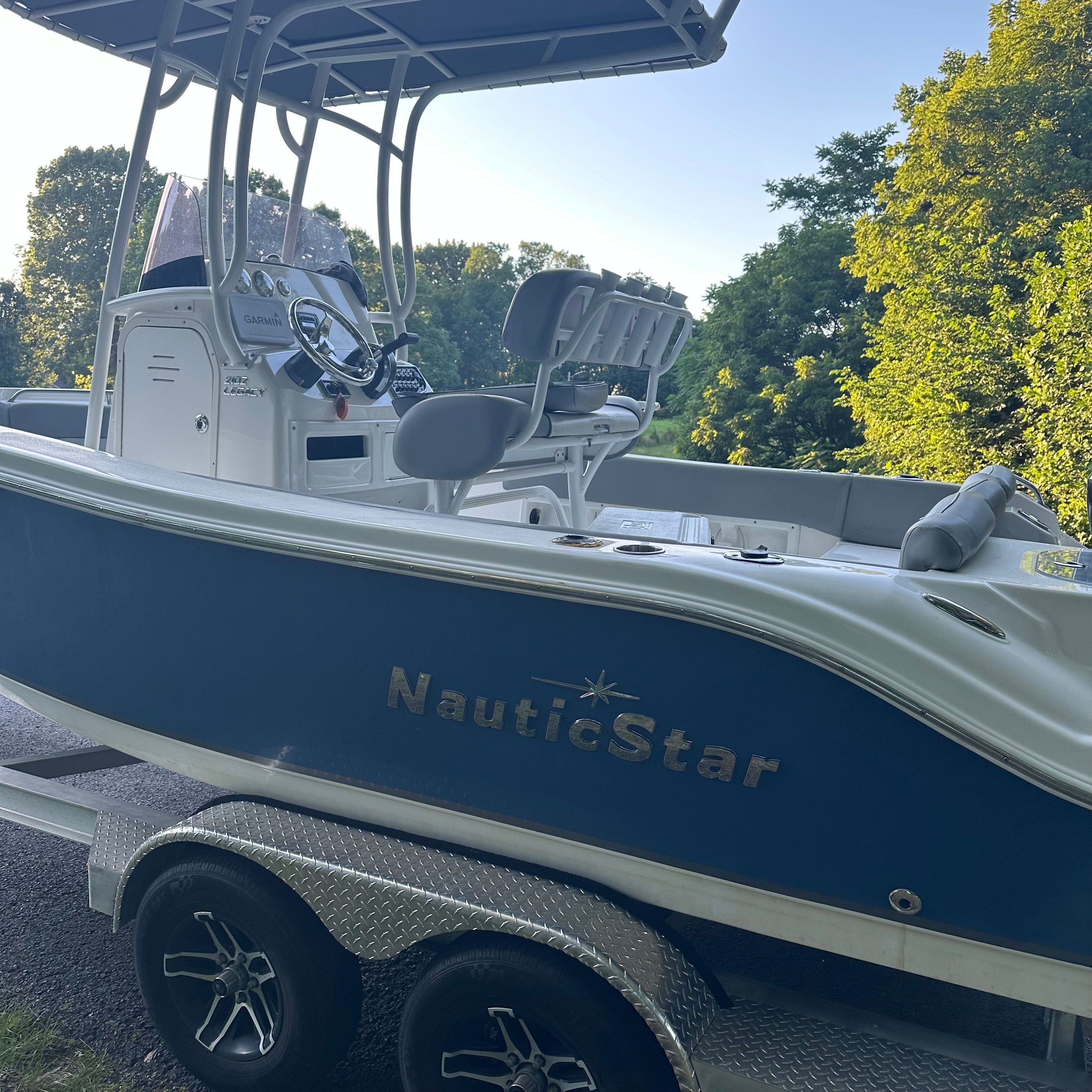 A 2022 NauticStar 2102 Legacy boat on a trailer, surrounded by trees.