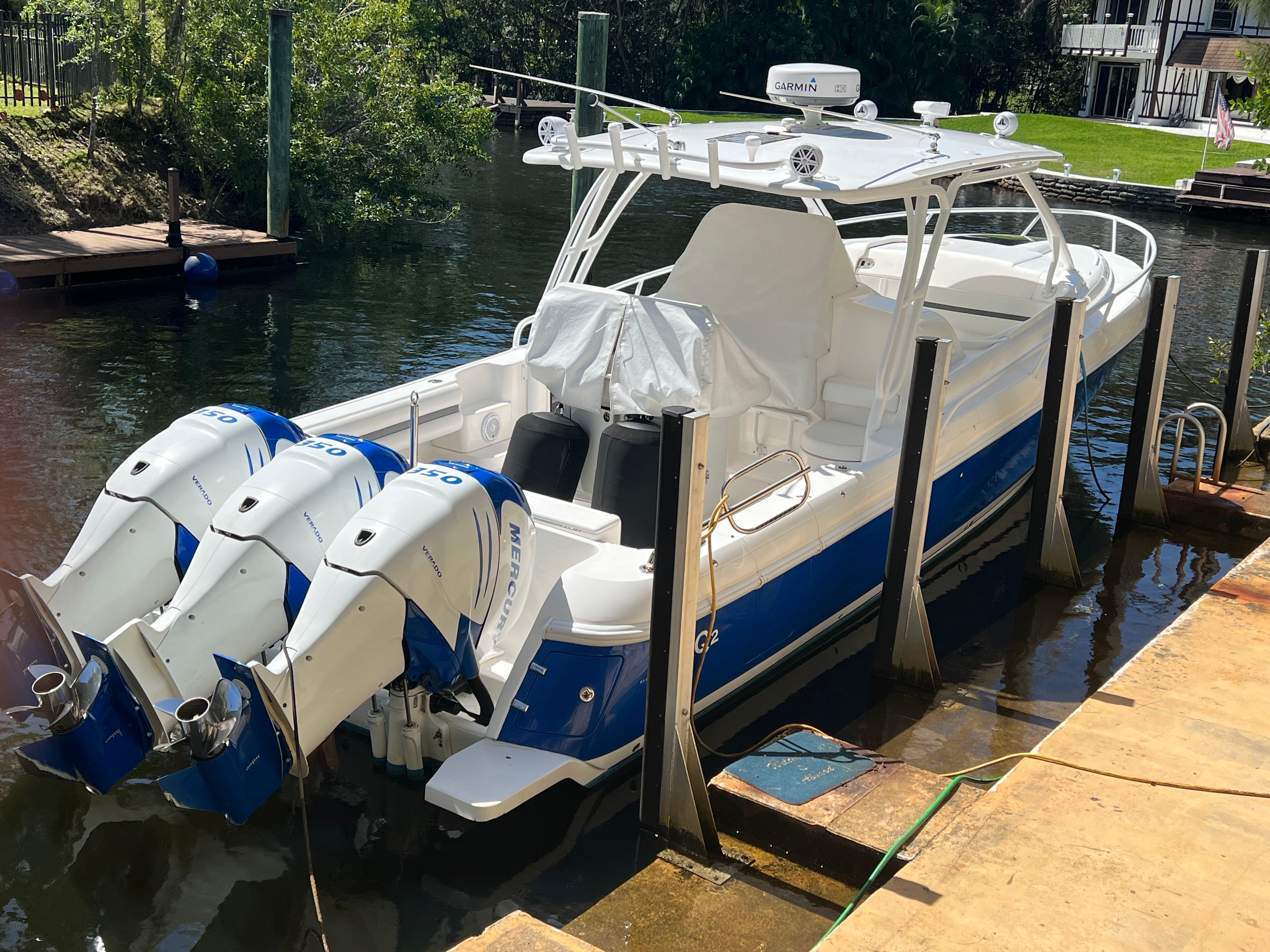 A 2014 Intrepid 375 Walkaround docked at a calm riverside, featuring three outboard engines.