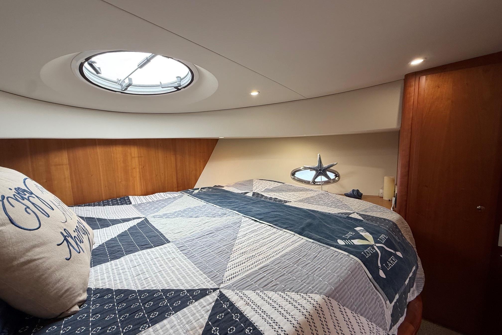 Cozy bedroom in 2004 Silverton 39 Motor Yacht with nautical decor and overhead porthole.
