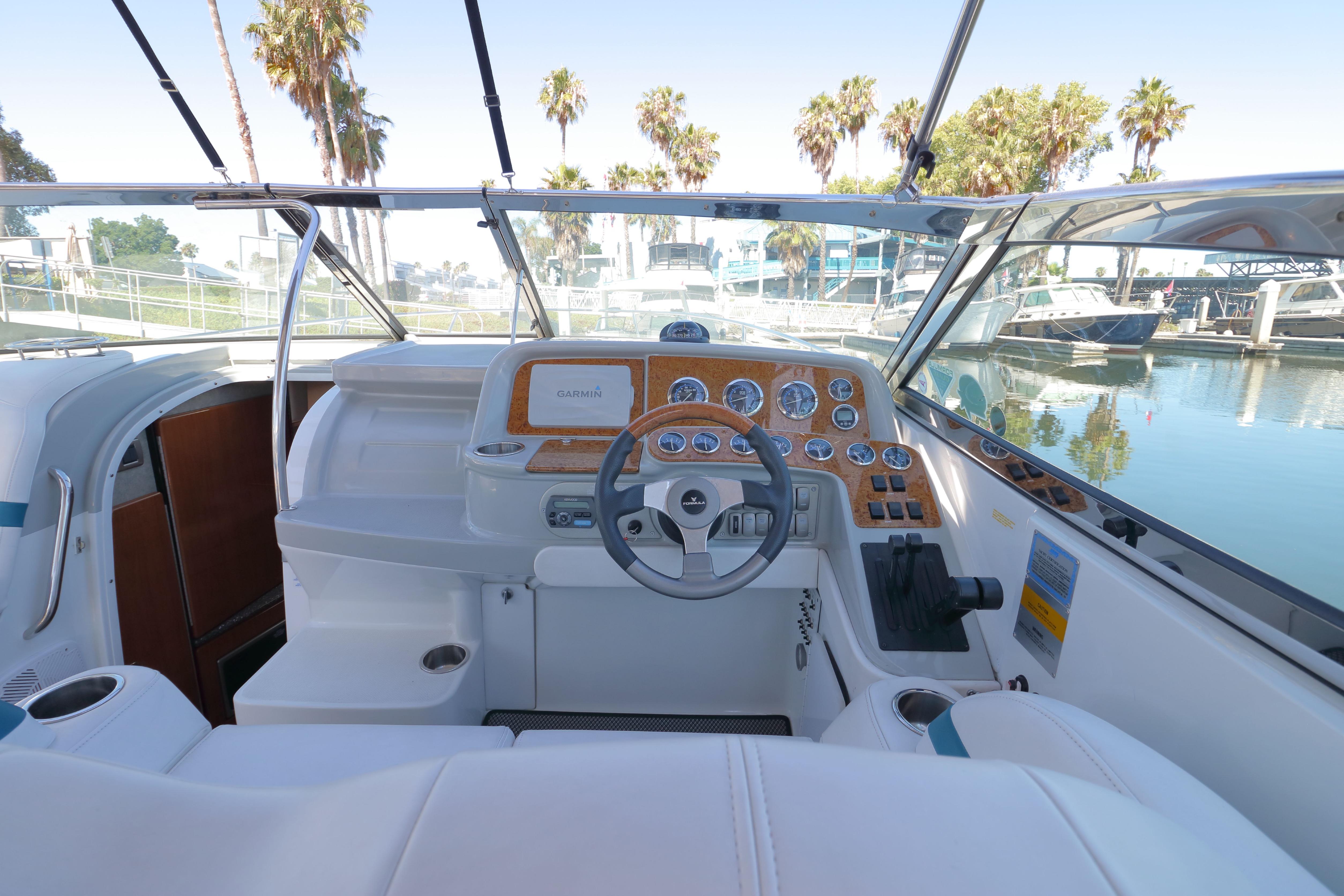 2006 Formula 330 Sun Sport boat cockpit with steering wheel and dashboard, docked near palm trees.