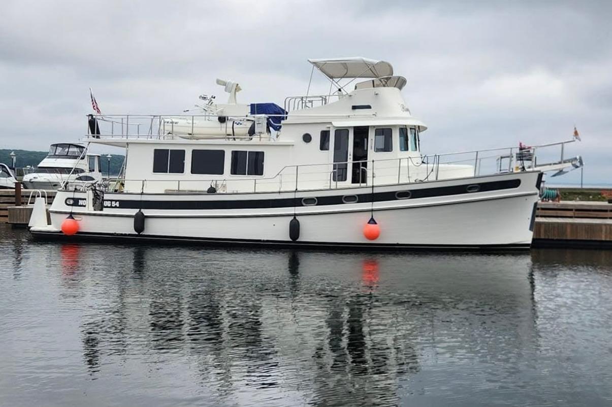 2007 Nordic Tug 54 yacht docked at marina, reflecting on calm water.