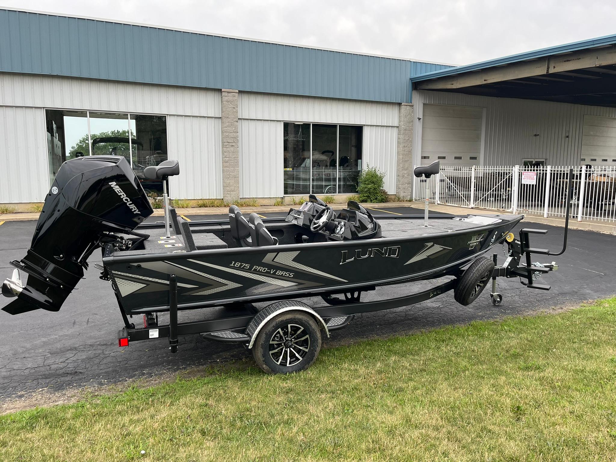 2026 Lund 1875 Pro-V Bass XS boat on trailer, parked outside a building.