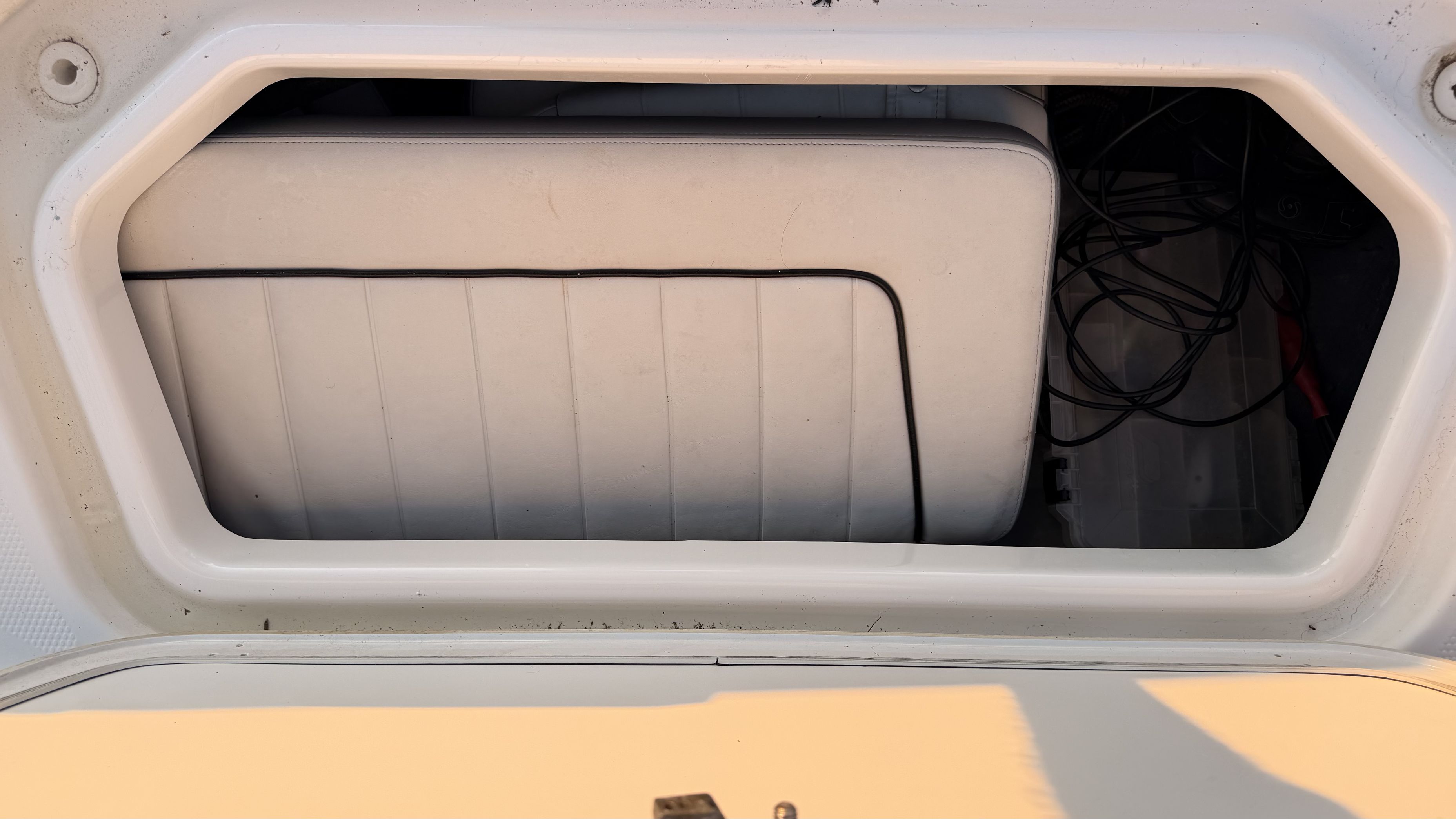 An open storage compartment on a boat with a white seat cushion and cables.