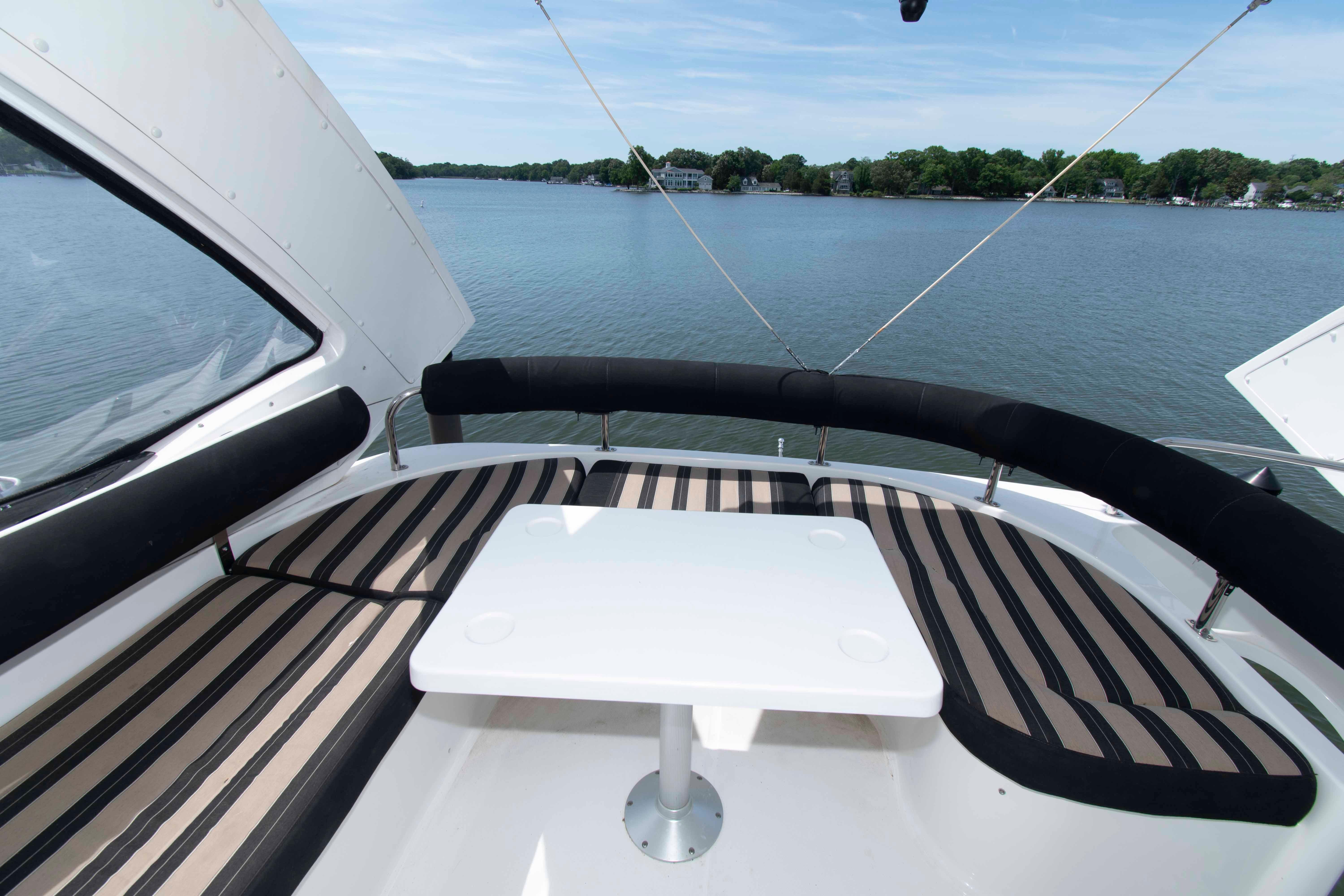Flybridge seating area on 2003 Neptunus 56 yacht overlooking serene water and lush shoreline.