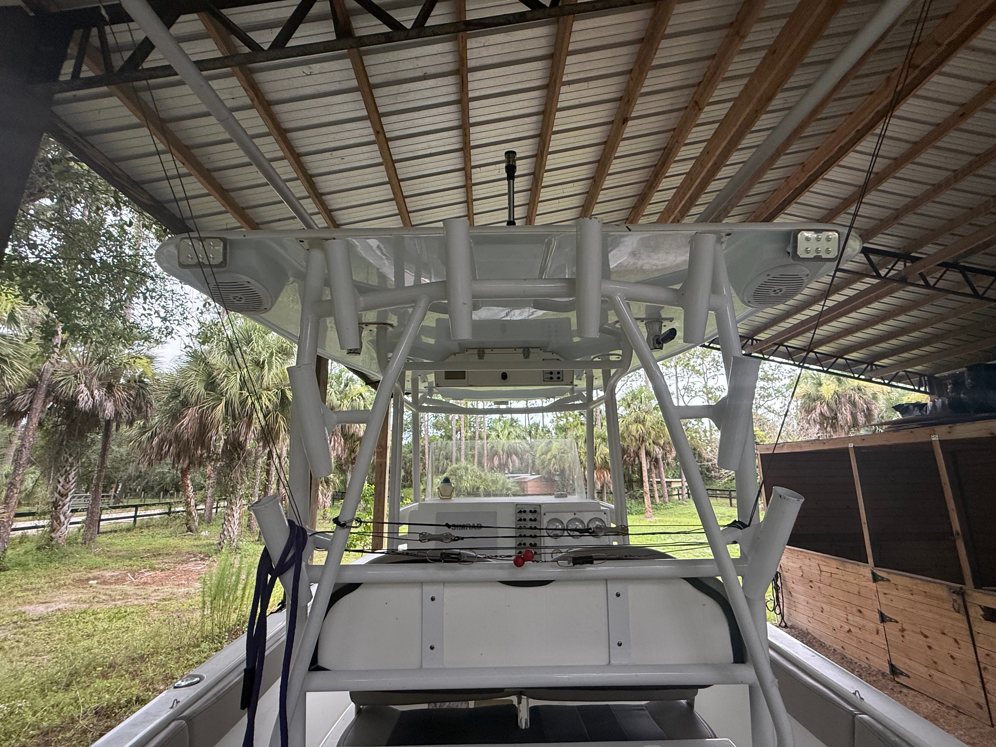 A 2021 Clearwater 2508 Center Console boat under a covered area, surrounded by trees.