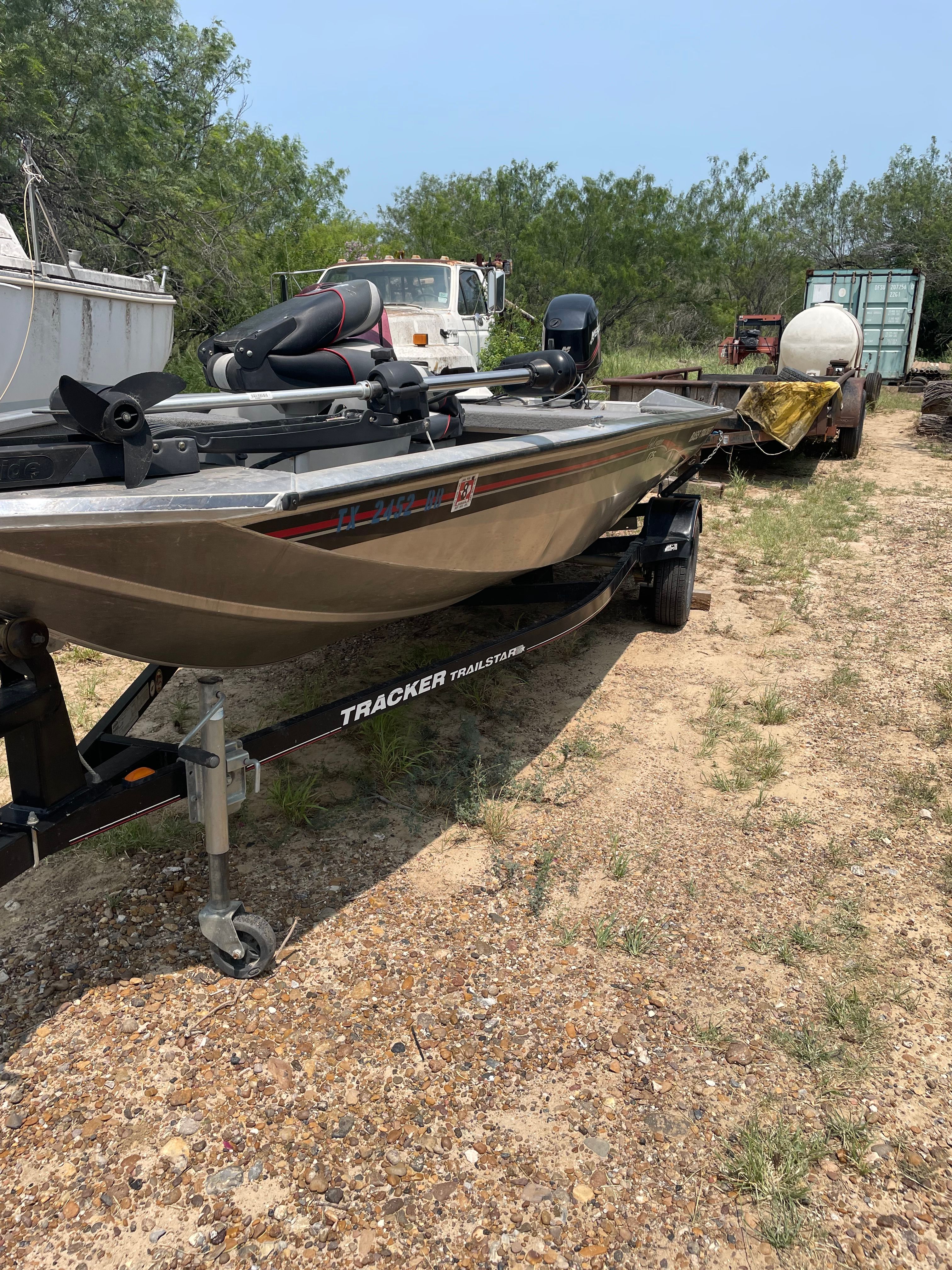 A 2009 Tracker Pro Crappie 175 on a trailer, surrounded by trees and vehicles.