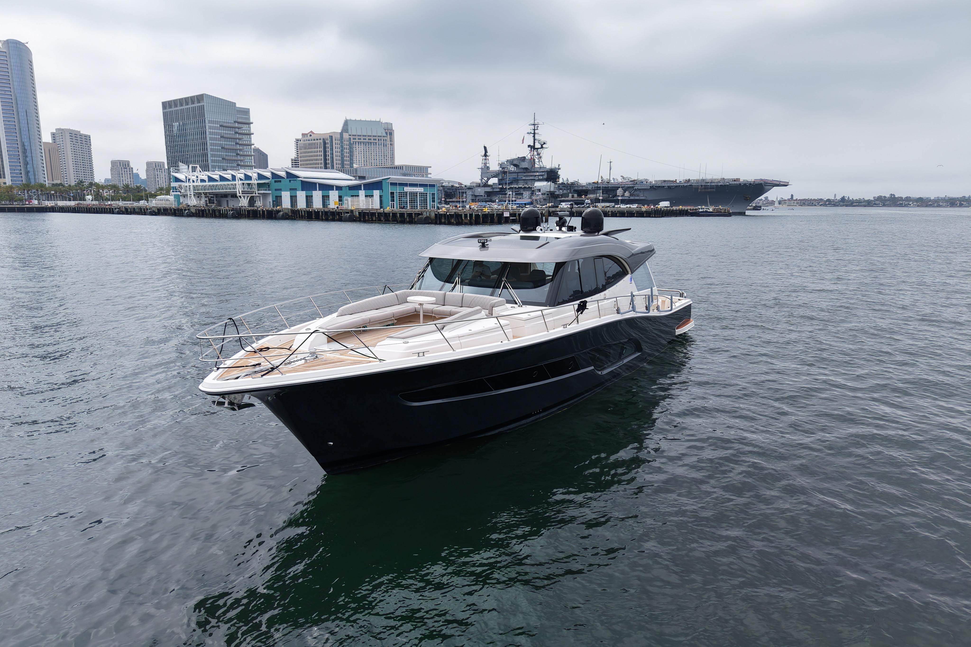 2023 Riviera 645 SUV yacht cruising near urban waterfront with city skyline backdrop.