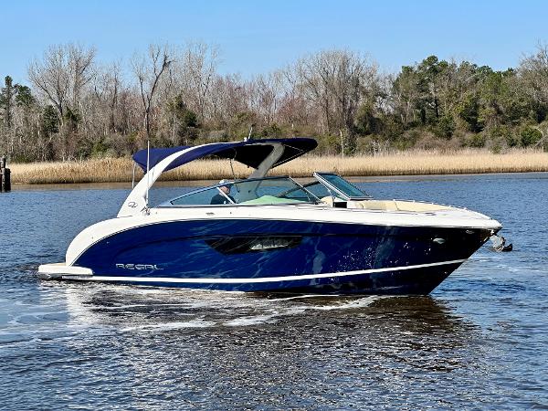 A blue and white motorboat cruises on a calm river, surrounded by trees.