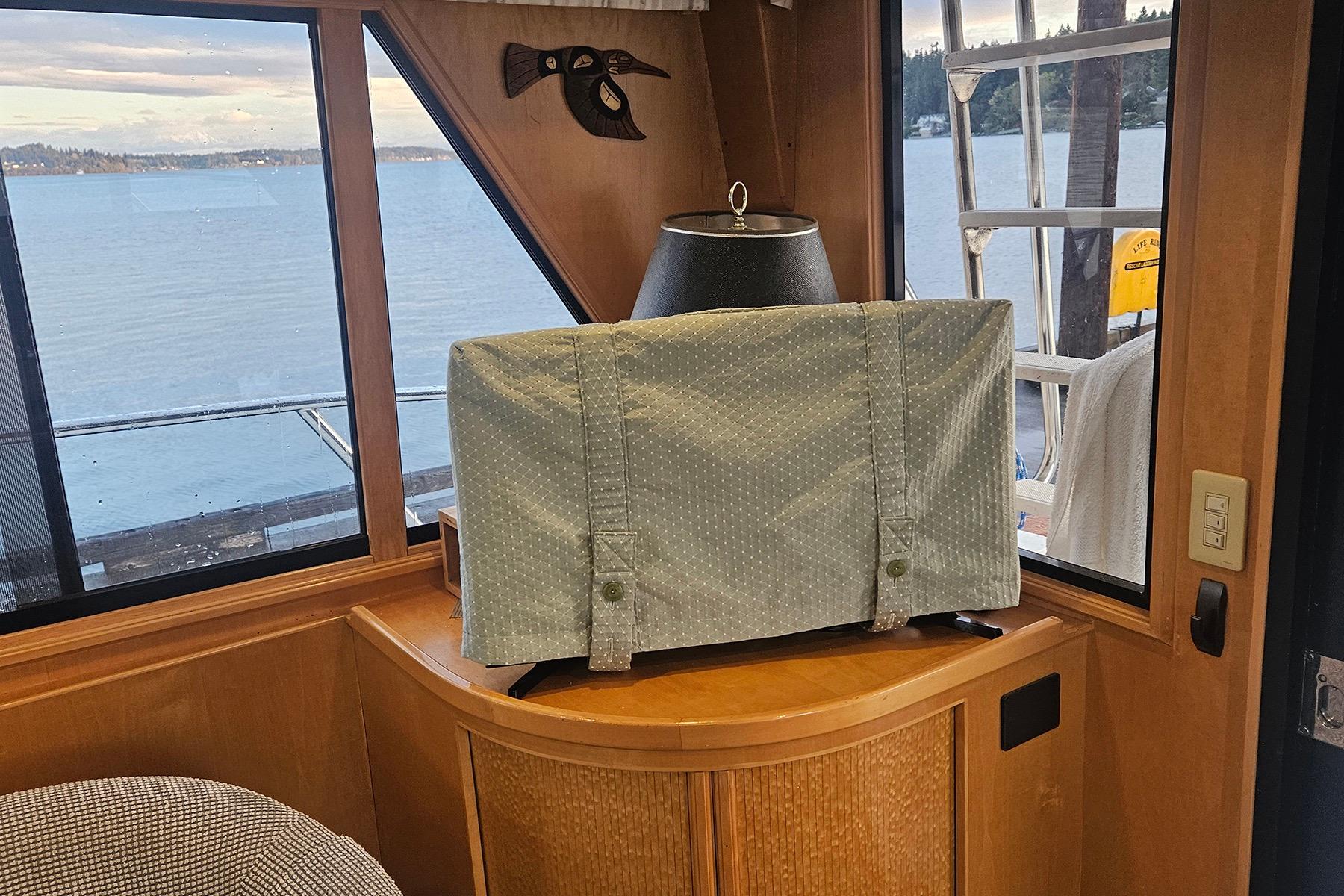 Cozy boat interior with covered TV, scenic lake view, and wooden decor.