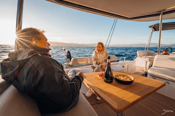 Couple enjoying sunset on Nautitech 44 Open yacht, 2025 model, with wine and snacks.