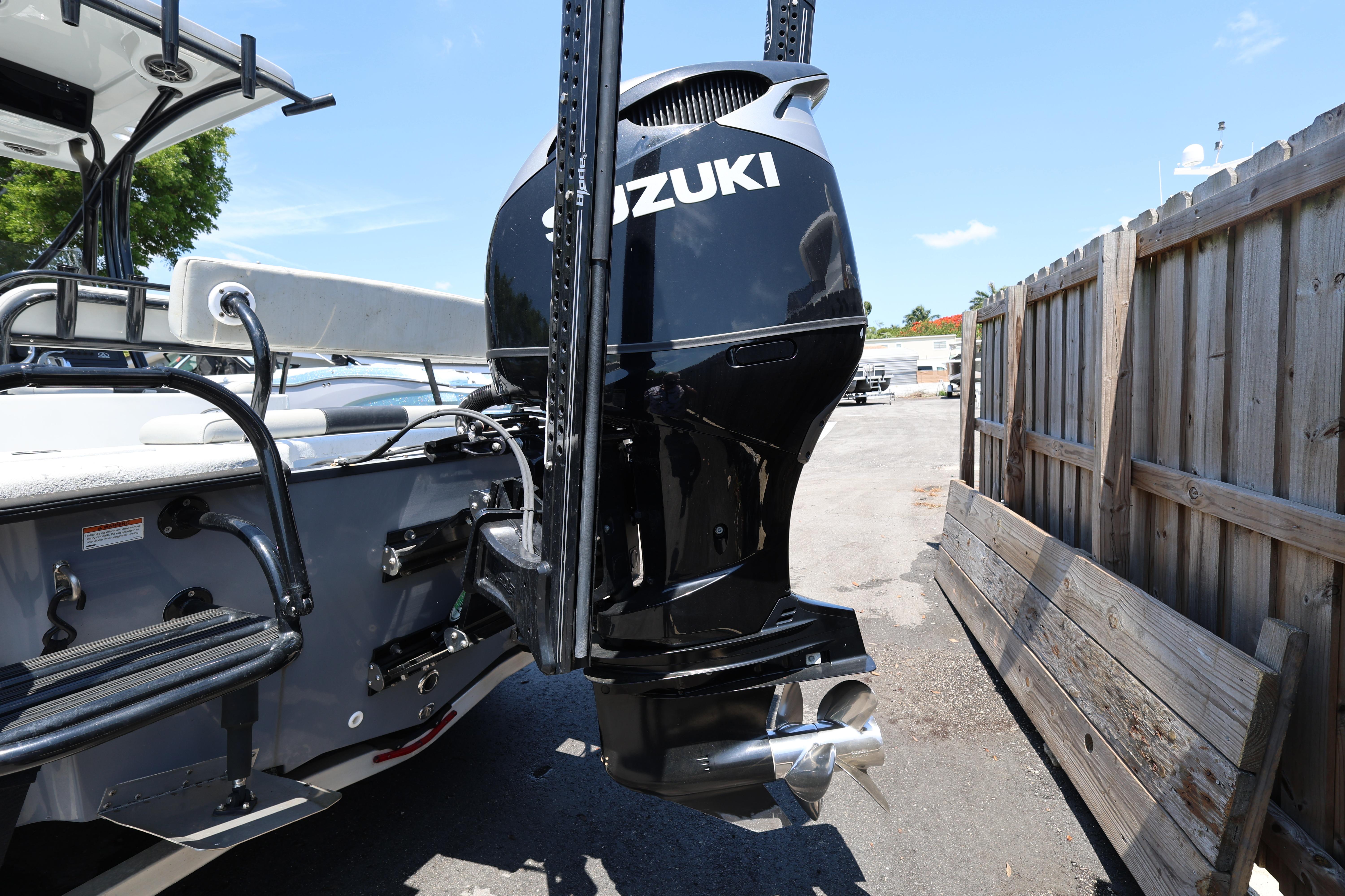 2021 Blazer Bay 2400 boat with Suzuki outboard motor, parked near wooden fence.