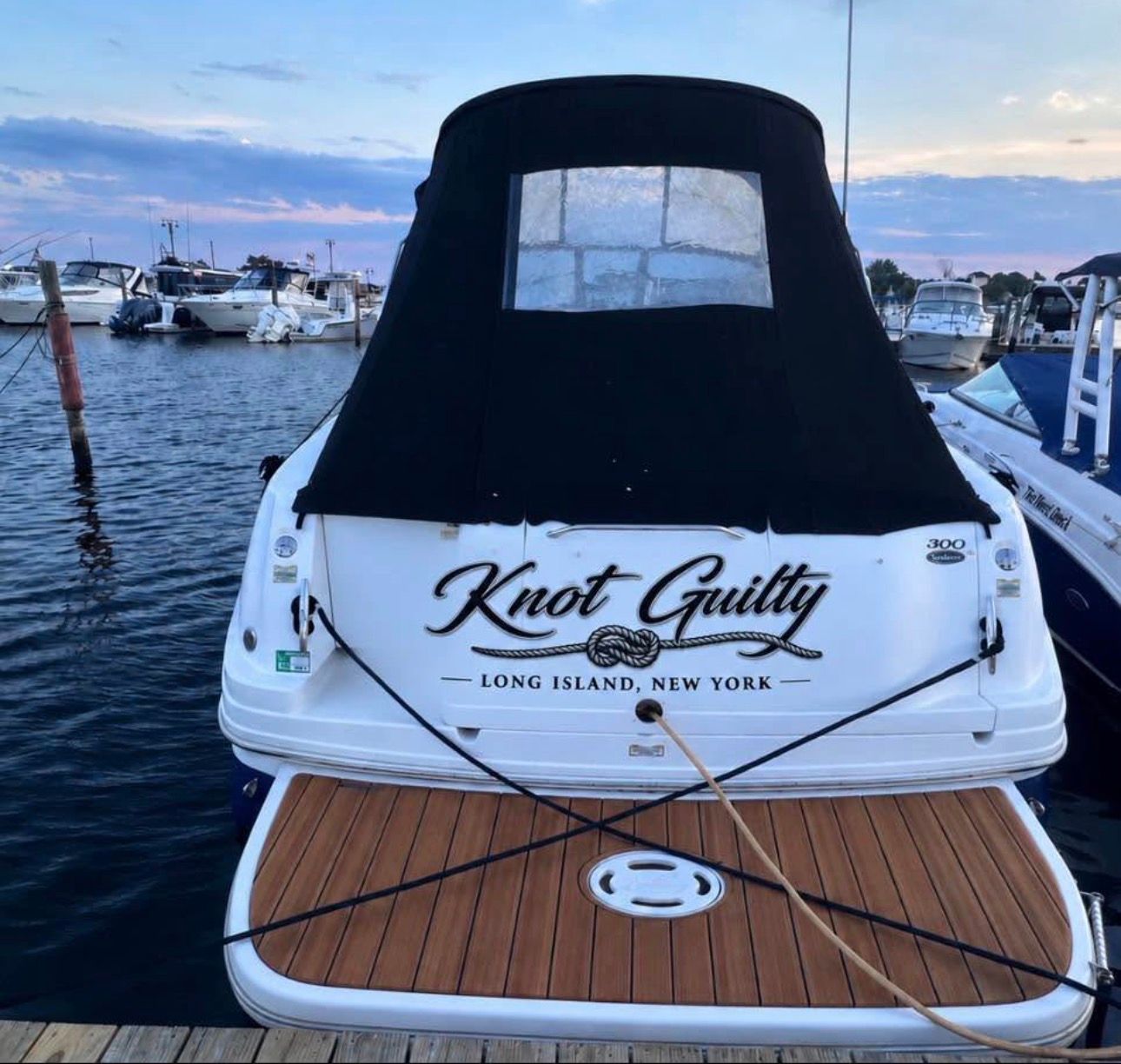 The stern of a 2002 Sea Ray 300 Sundancer named "Knot Guilty" docked at a marina.