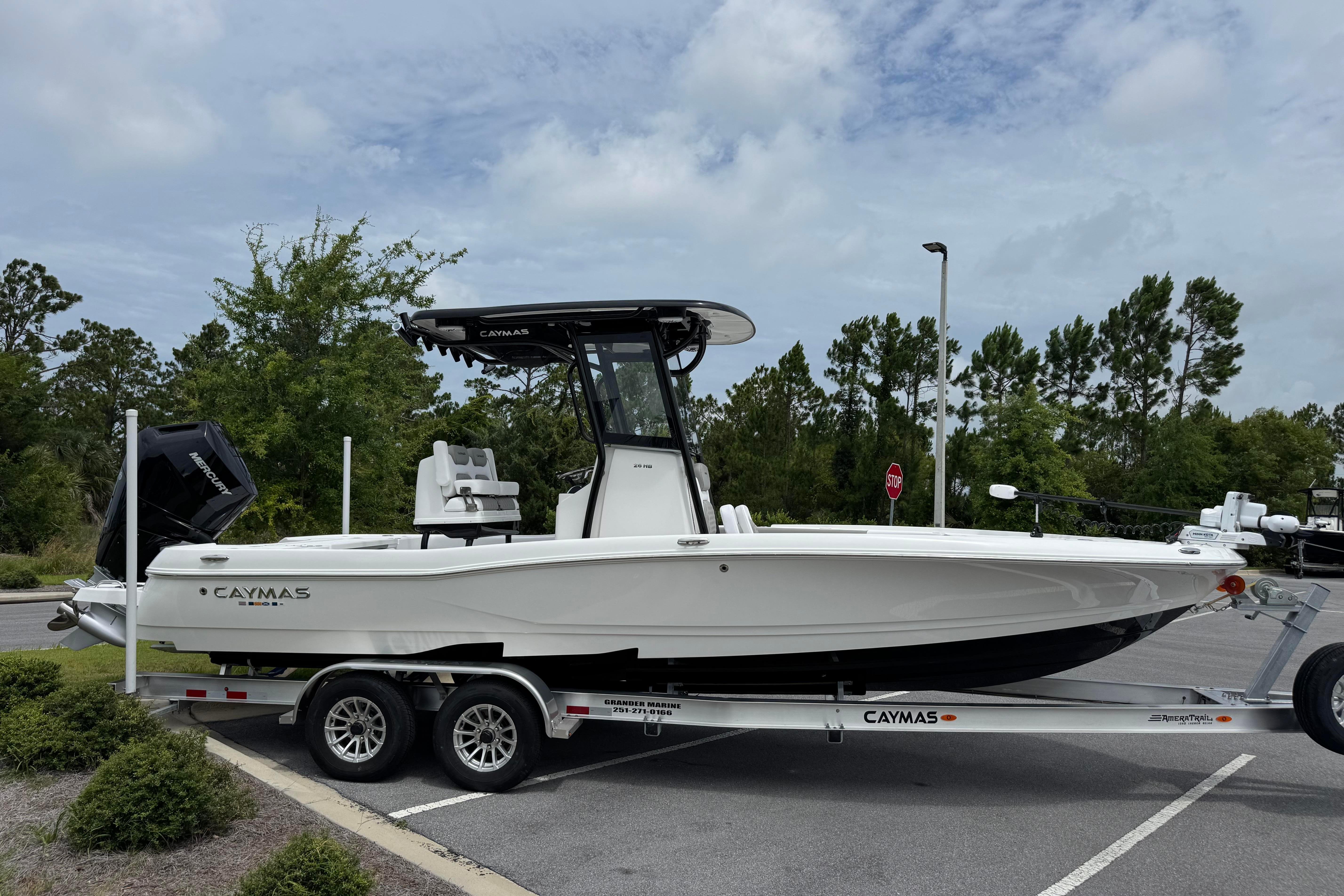 2027 Caymas 26 HB boat on trailer in parking lot, surrounded by trees.
