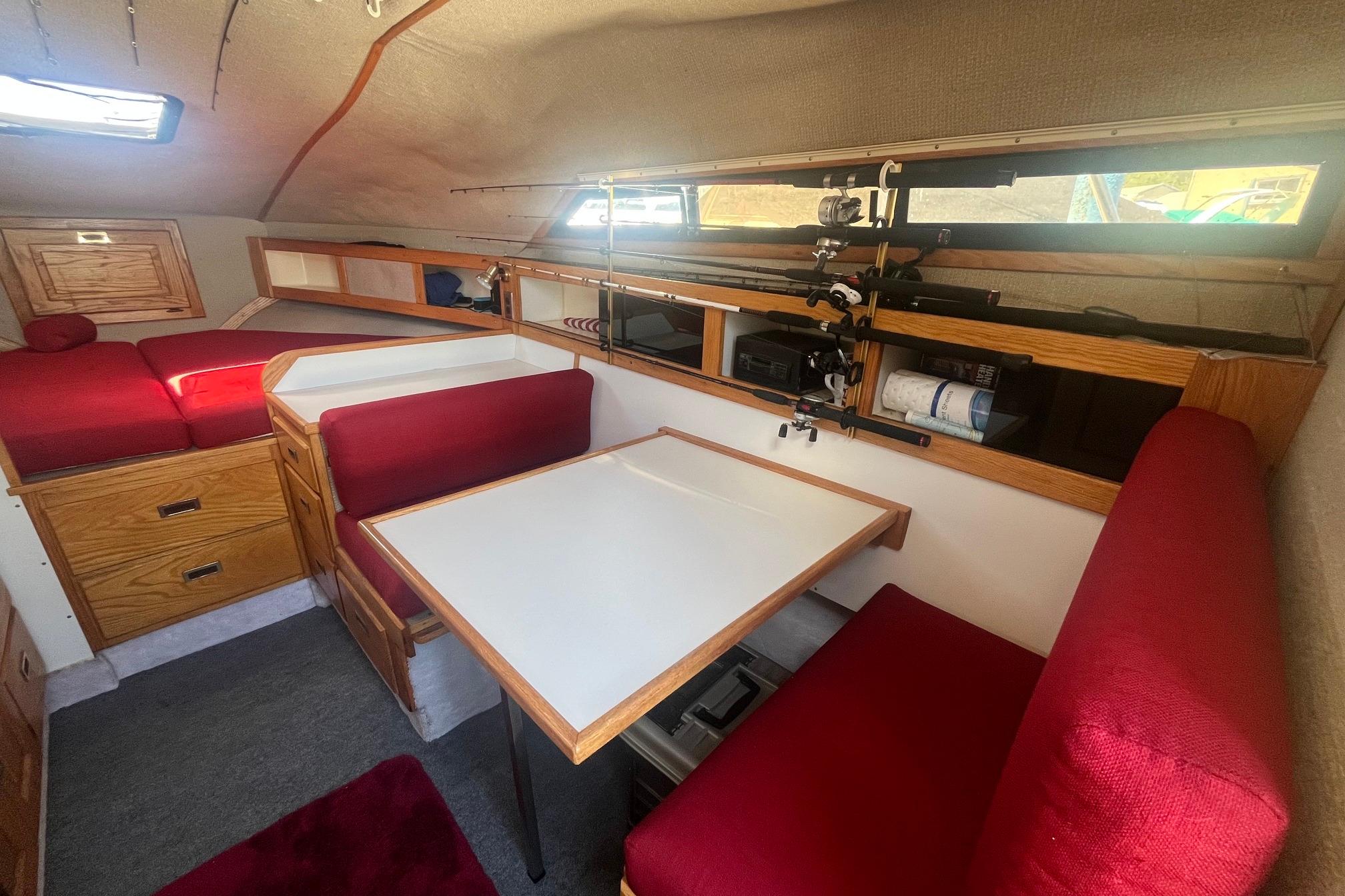 Interior of 1988 Seafox 29 Flybridge with red seating, dining table, and fishing rod storage.