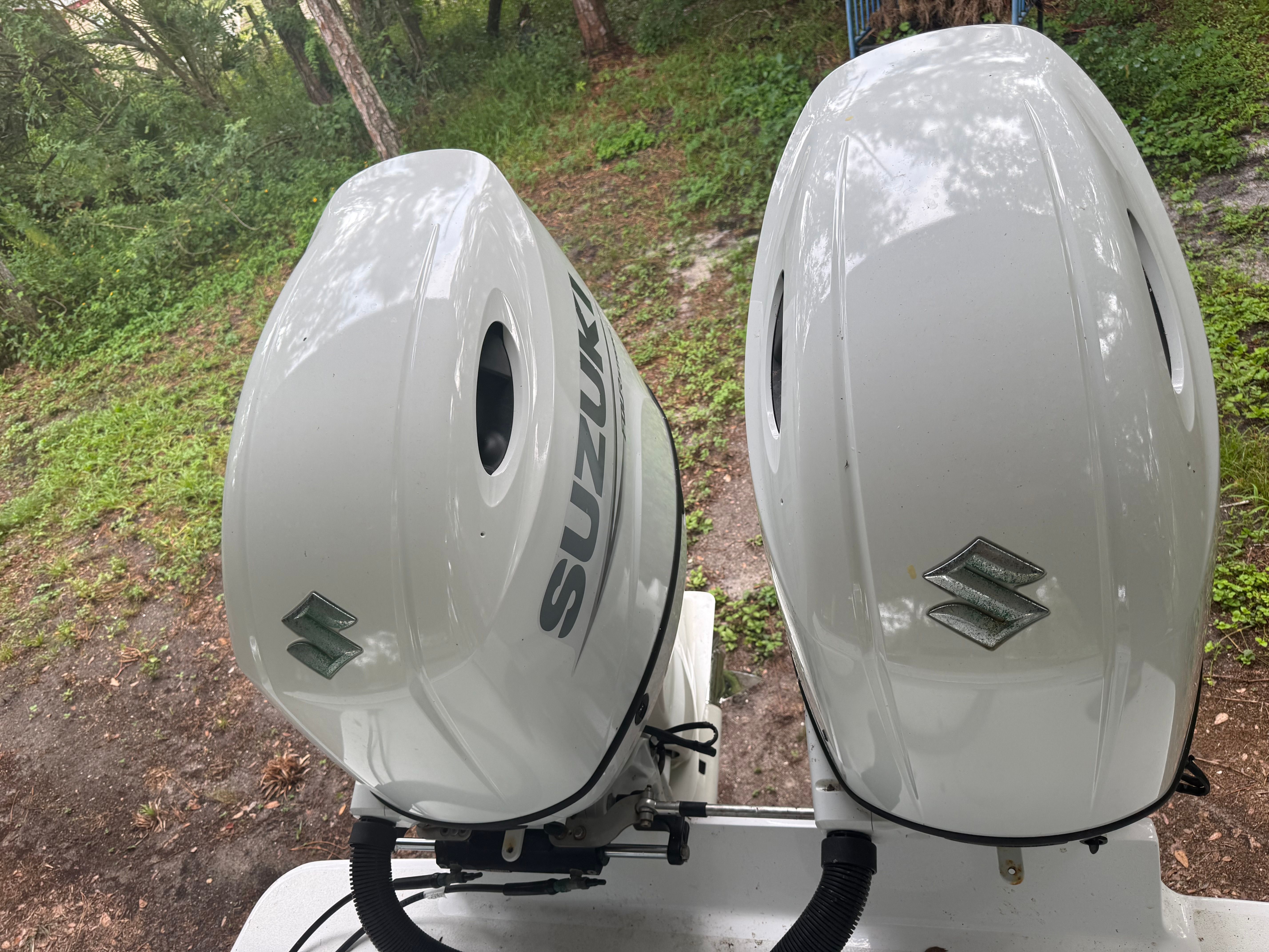 Two Suzuki outboard motors mounted on a boat, surrounded by a wooded area.