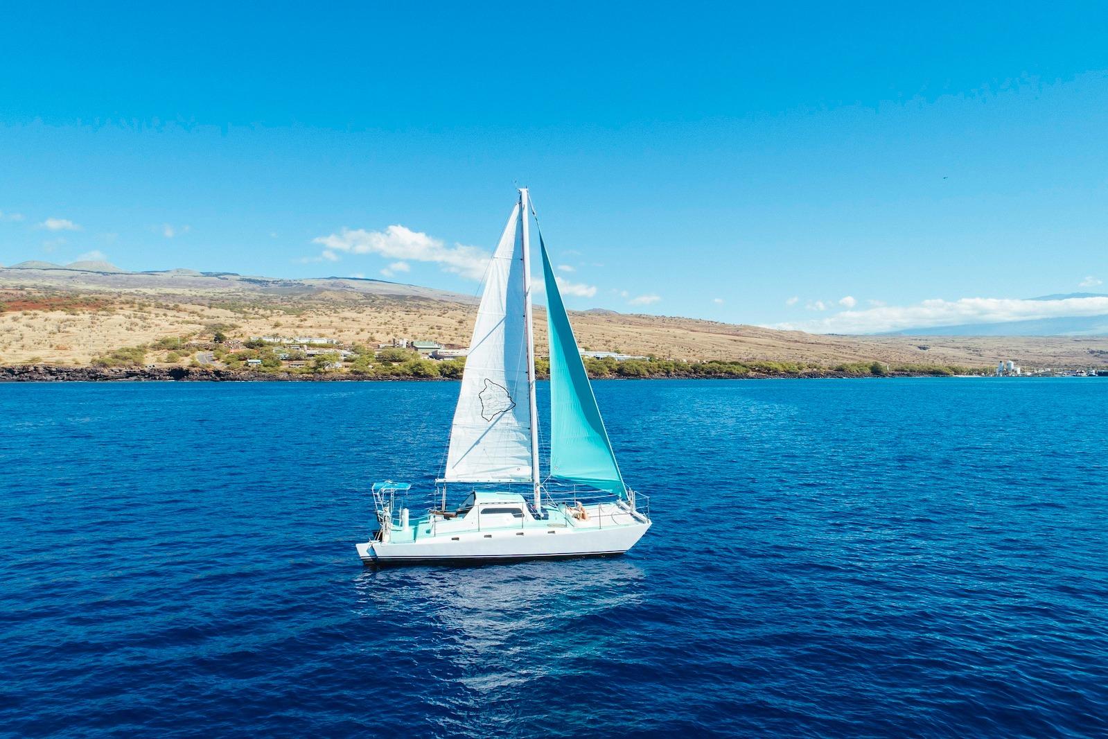 Sailboat "CSK Beach Cat" 1978 on blue ocean near scenic coastline under clear sky.