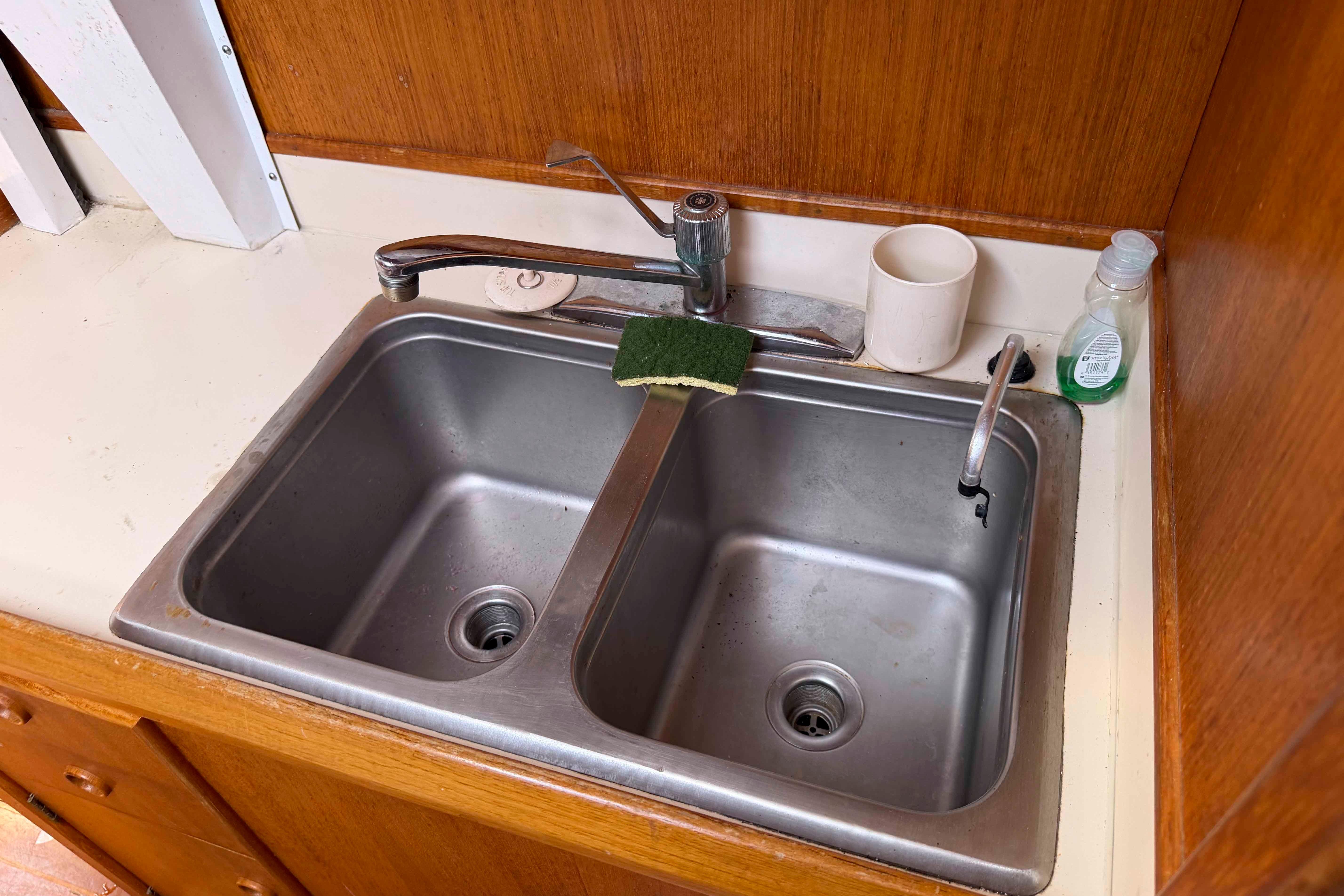 Double sink in 1983 Hinterhoeller Niagara 35 yacht galley with faucet and cleaning supplies.