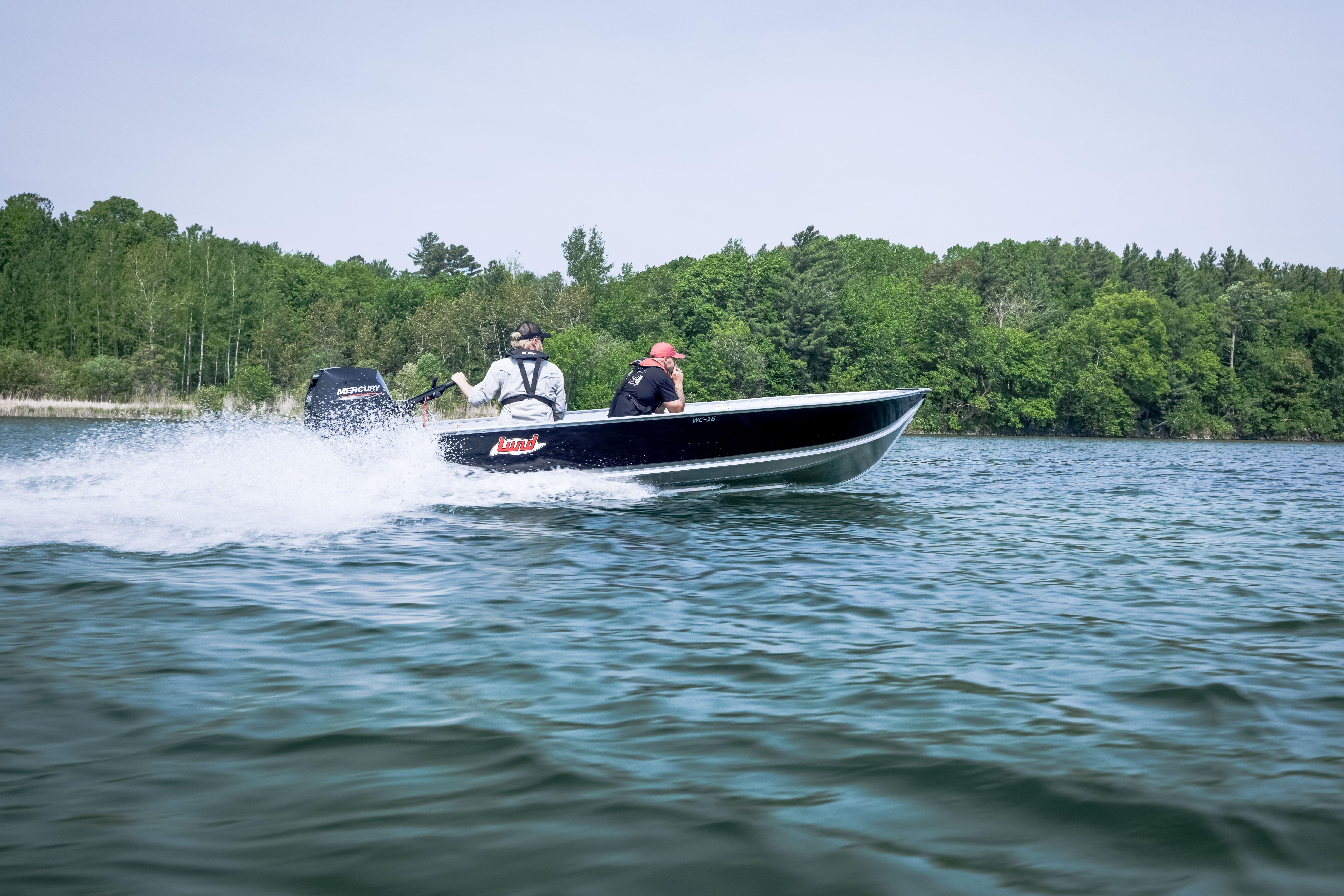 2027 Lund WC 16 boat speeding on a lake with lush green forest backdrop.