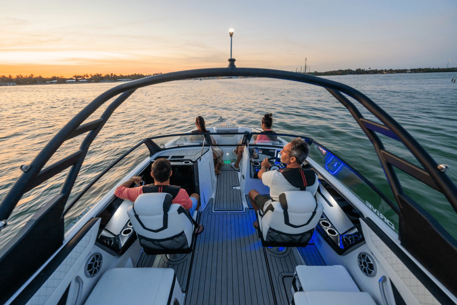 Four people sit in a modern boat on calm water at sunset.