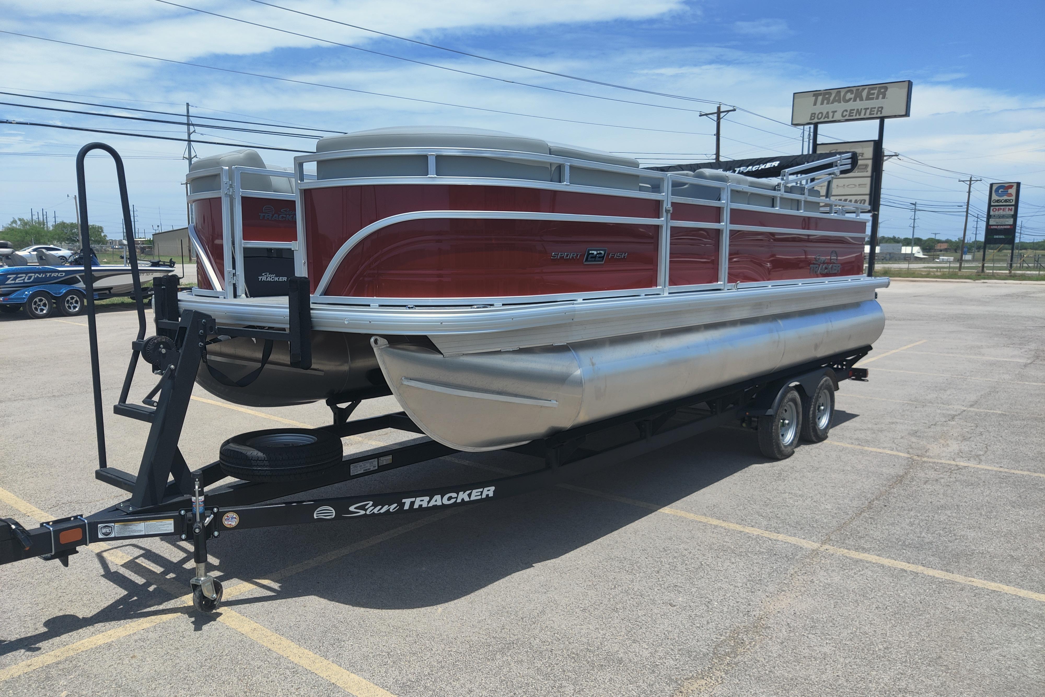 2026 Sun Tracker SportFish 22 DLX pontoon boat on trailer in parking lot.