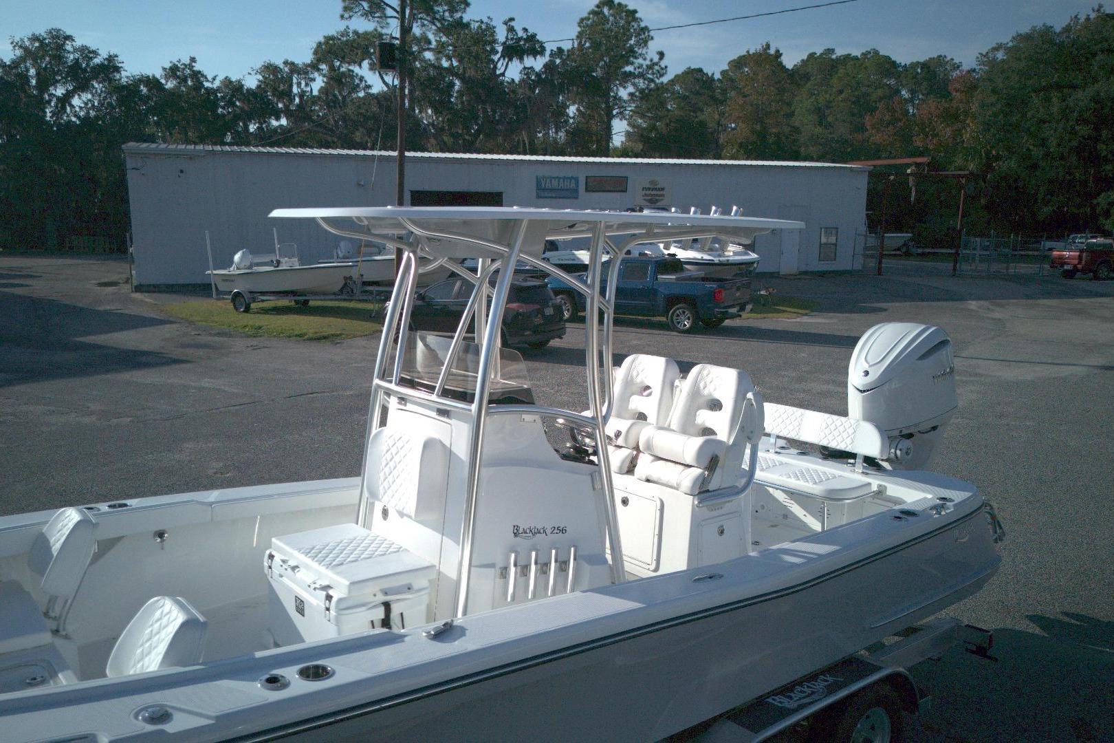 2026 BlackJack 256 Coastal boat with T-top and outboard motor in a parking lot.