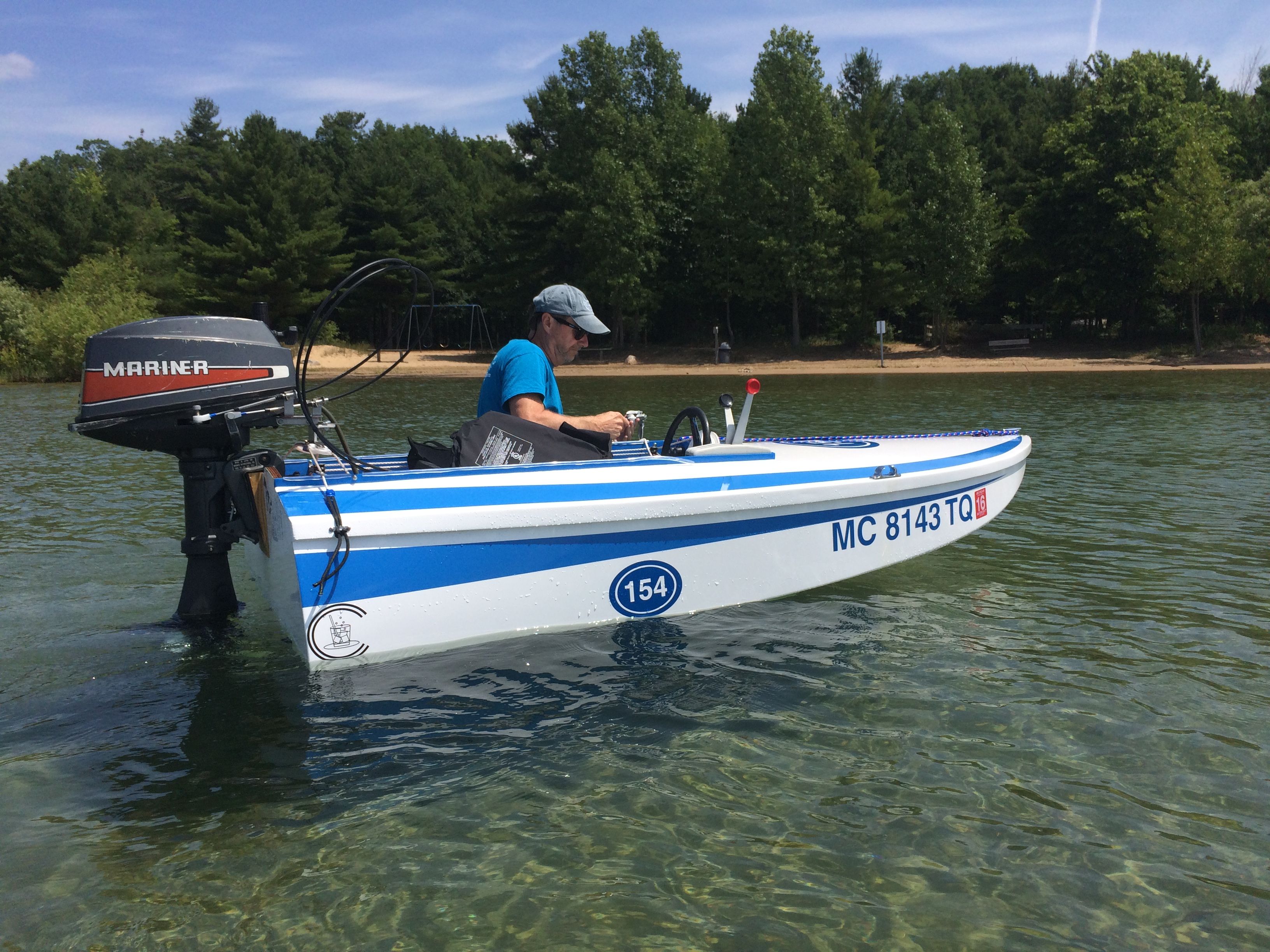 A man operates a small blue and white boat with an outboard motor on a calm lake.