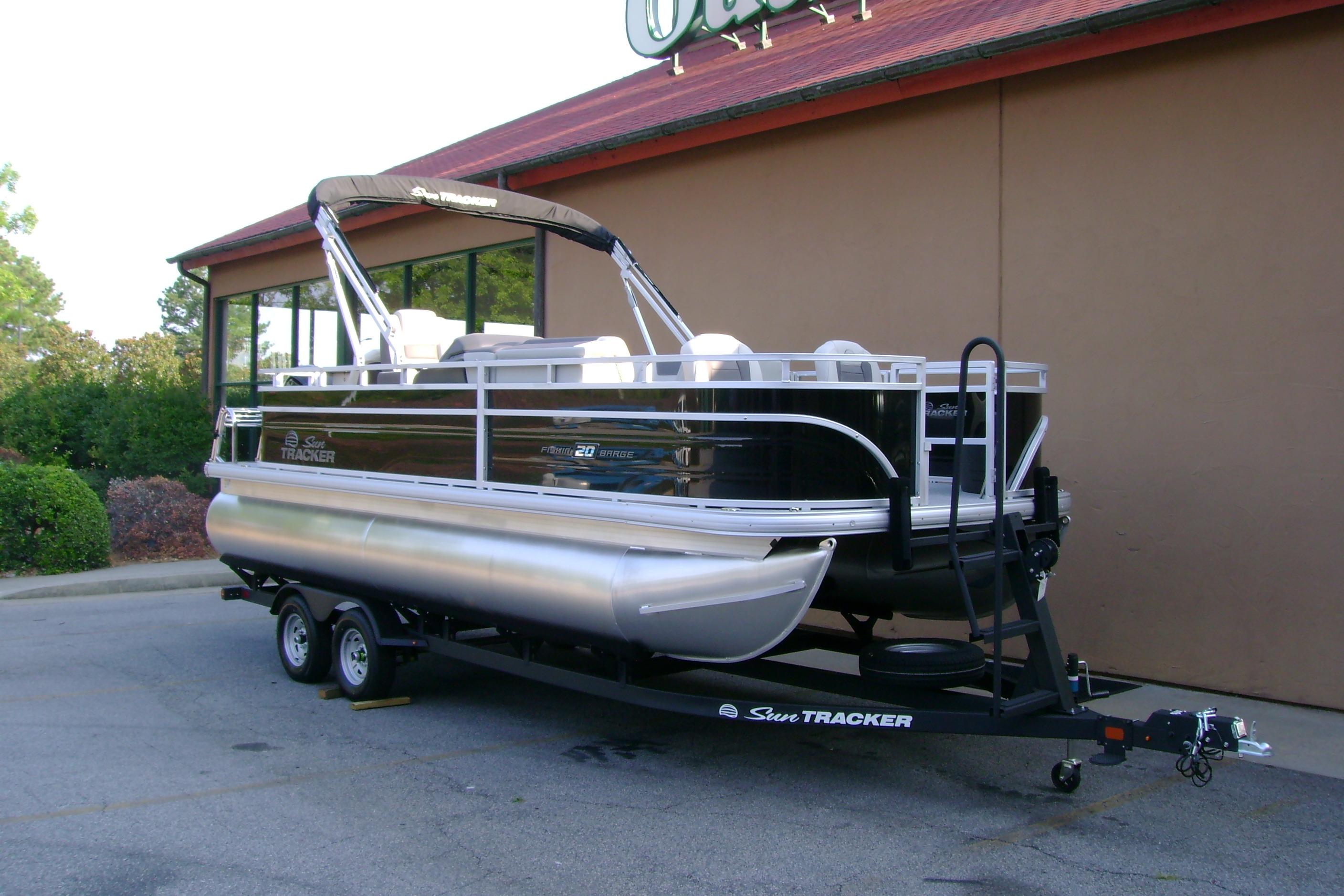 2026 Sun Tracker Fishin' Barge 20 DLX pontoon boat on trailer, parked outdoors.