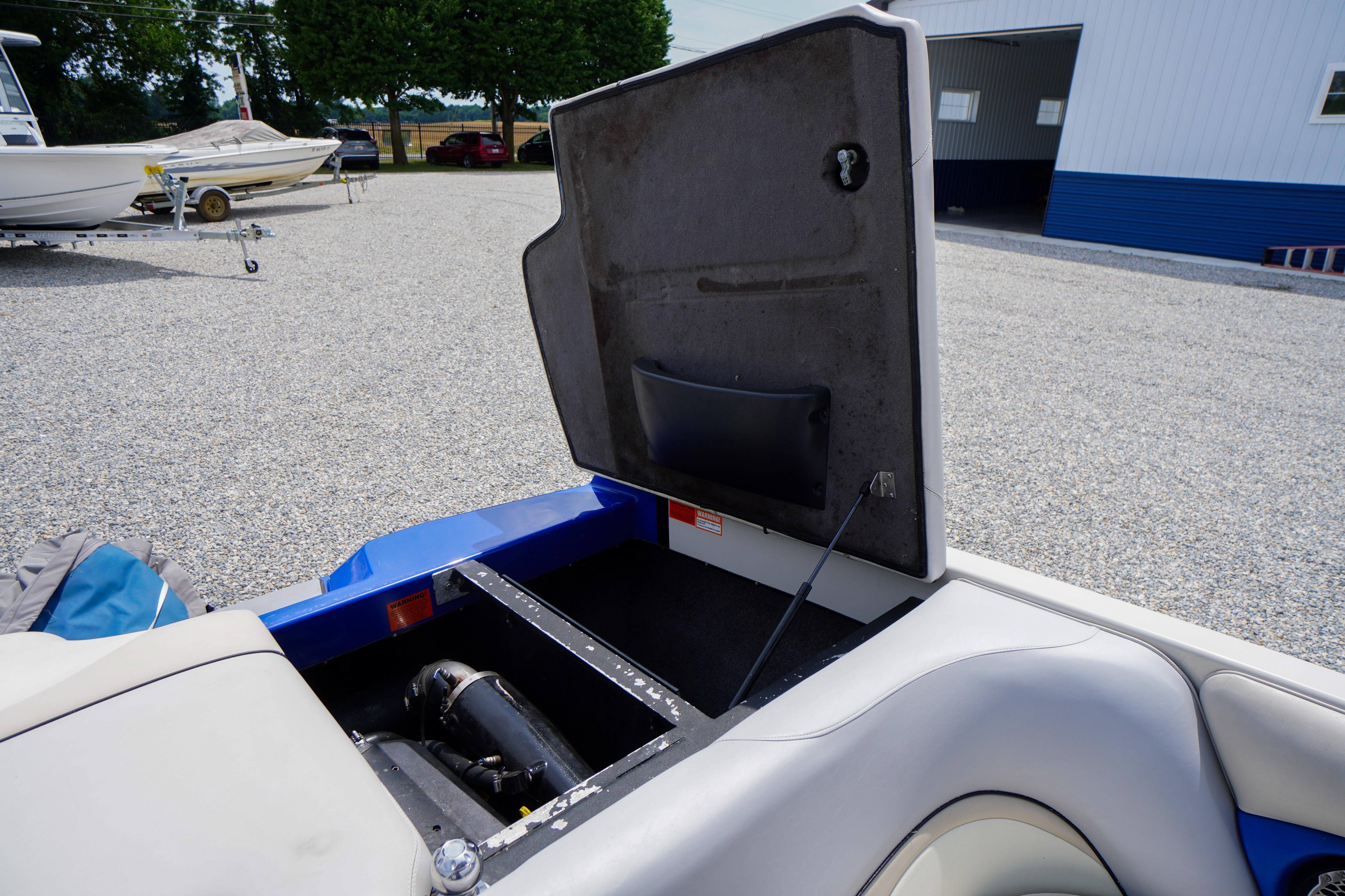 Open storage compartment of a 2011 Malibu Wakesetter 21 VLX boat in a gravel lot.