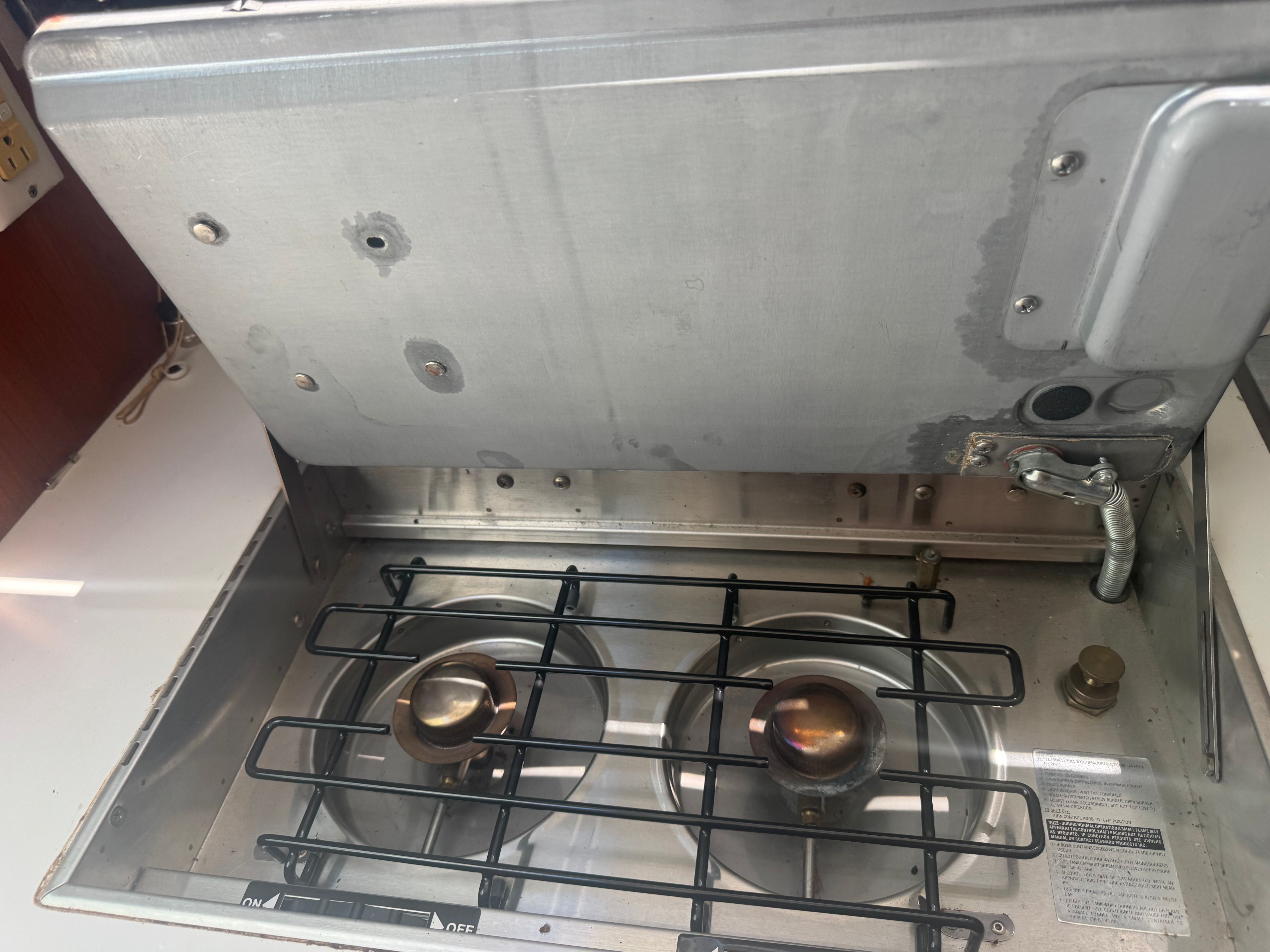 A two-burner stove in a boat's galley, surrounded by metal surfaces.