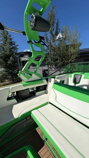Green and white boat with cushioned seats and speakers, surrounded by trees.