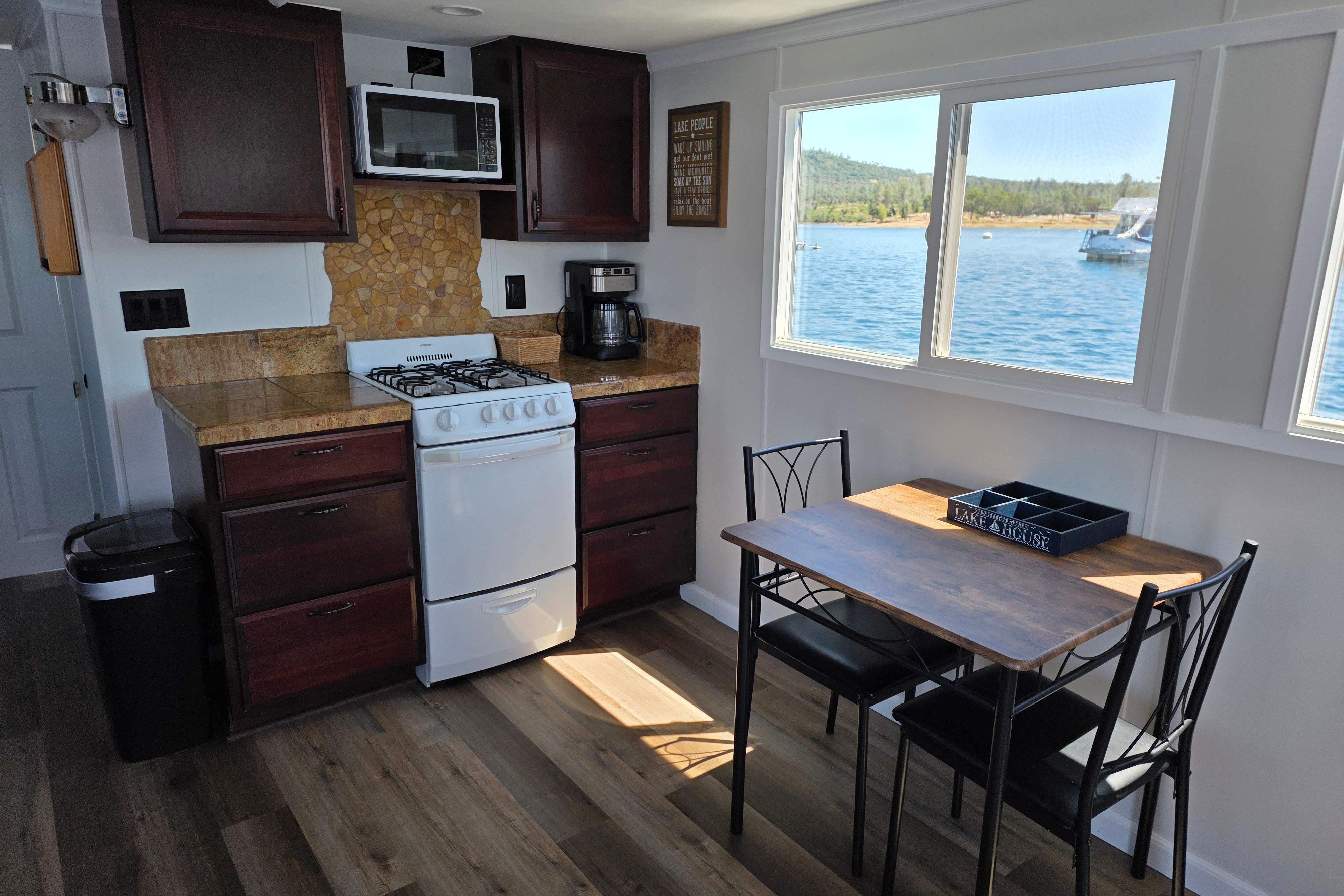 Cozy 2007 custom houseboat kitchen with lake view, featuring stove, microwave, and dining area.