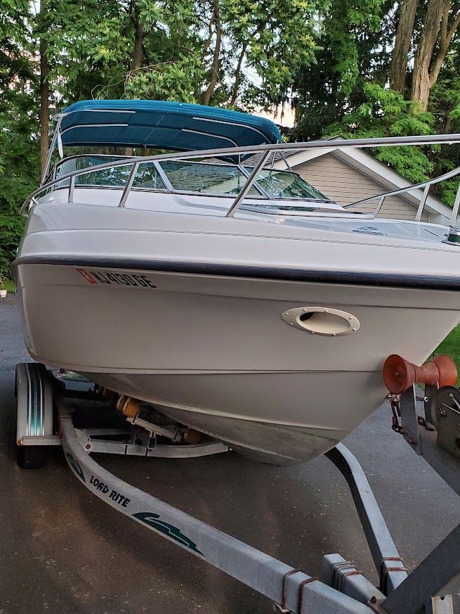 A 1998 Crownline 210 CCR boat on a trailer, surrounded by trees.