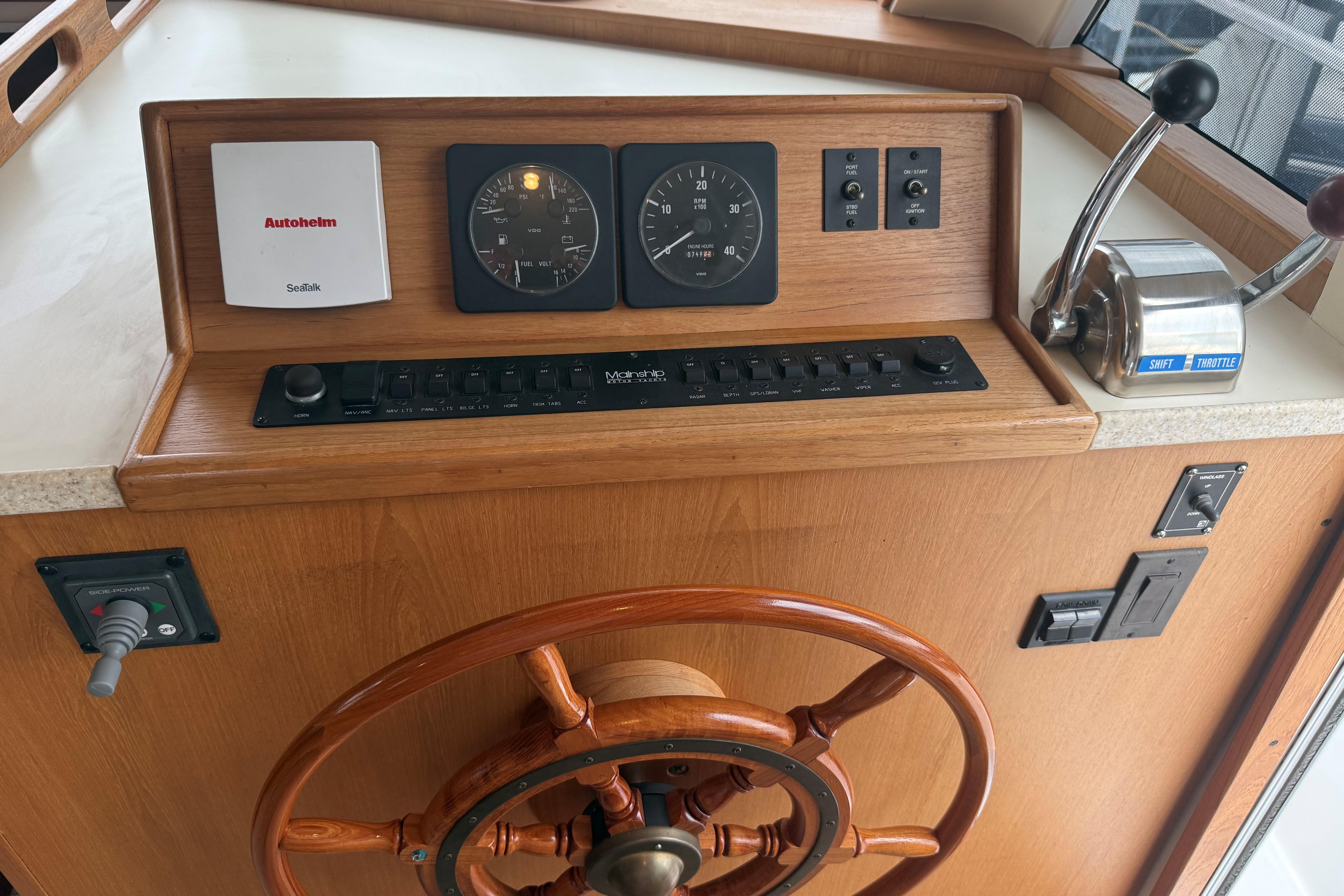 1999 Mainship 350 Trawler helm with wooden wheel, gauges, and throttle controls.
