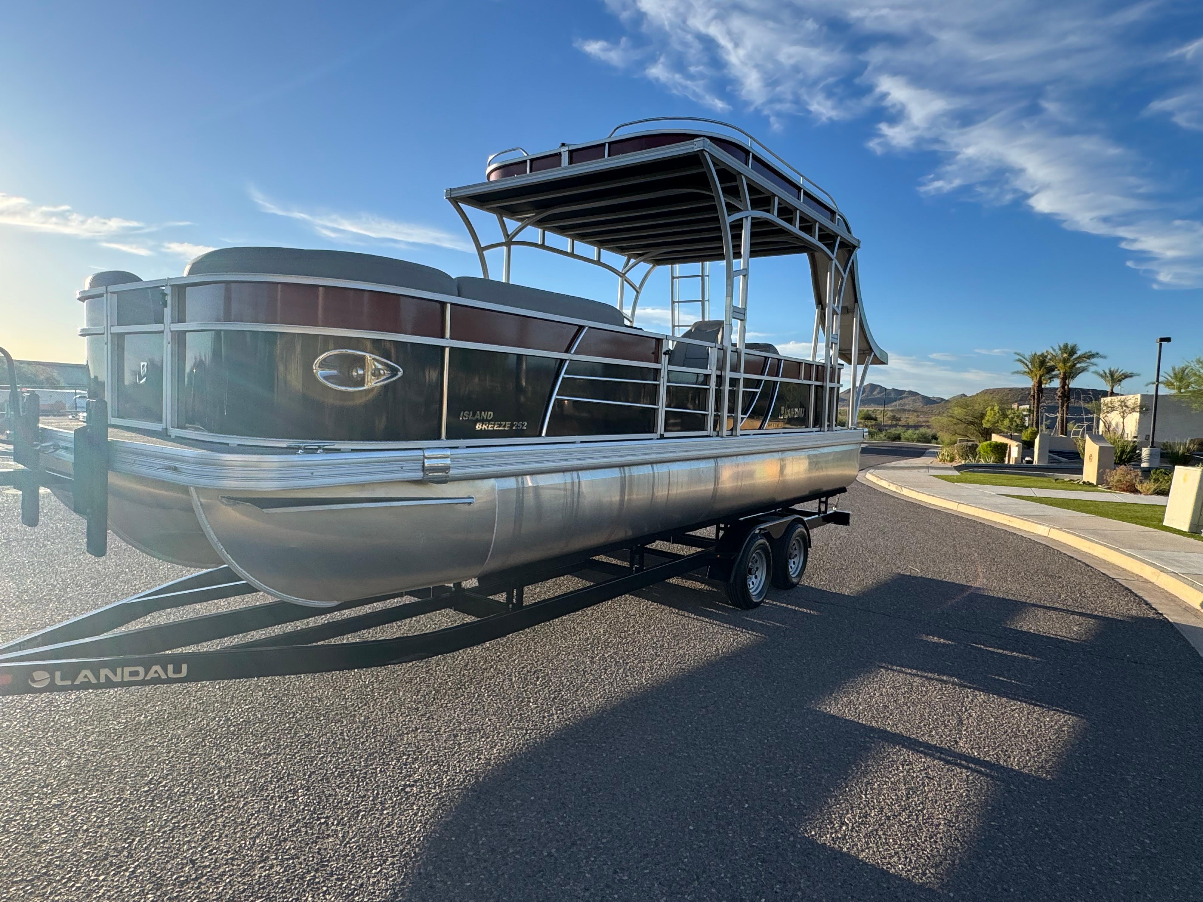 2024 Landau Island Breeze 252 pontoon boat on trailer, parked on sunny street.