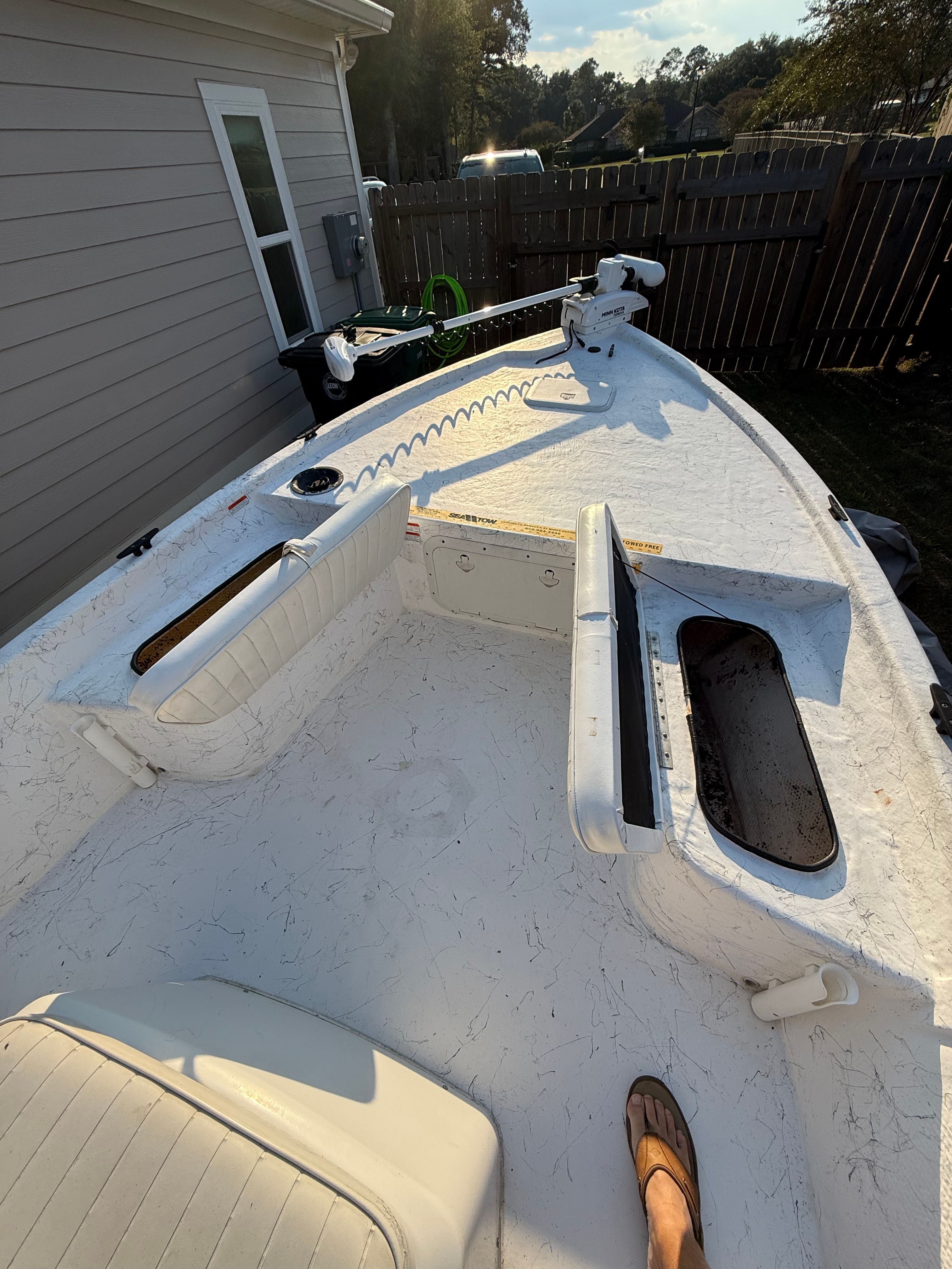 A white boat with seating and storage compartments is in a fenced yard.
