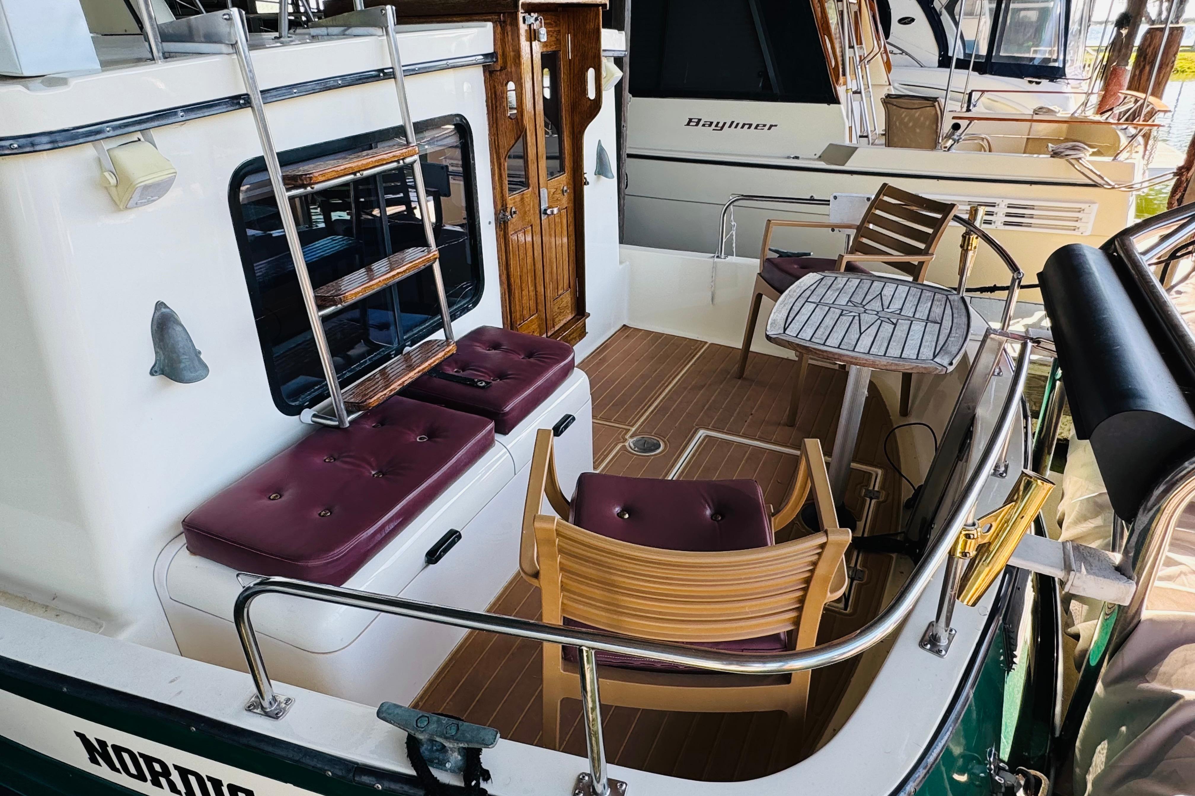 1996 Nordic Tug 32 boat deck with seating, table, and ladder in marina setting.