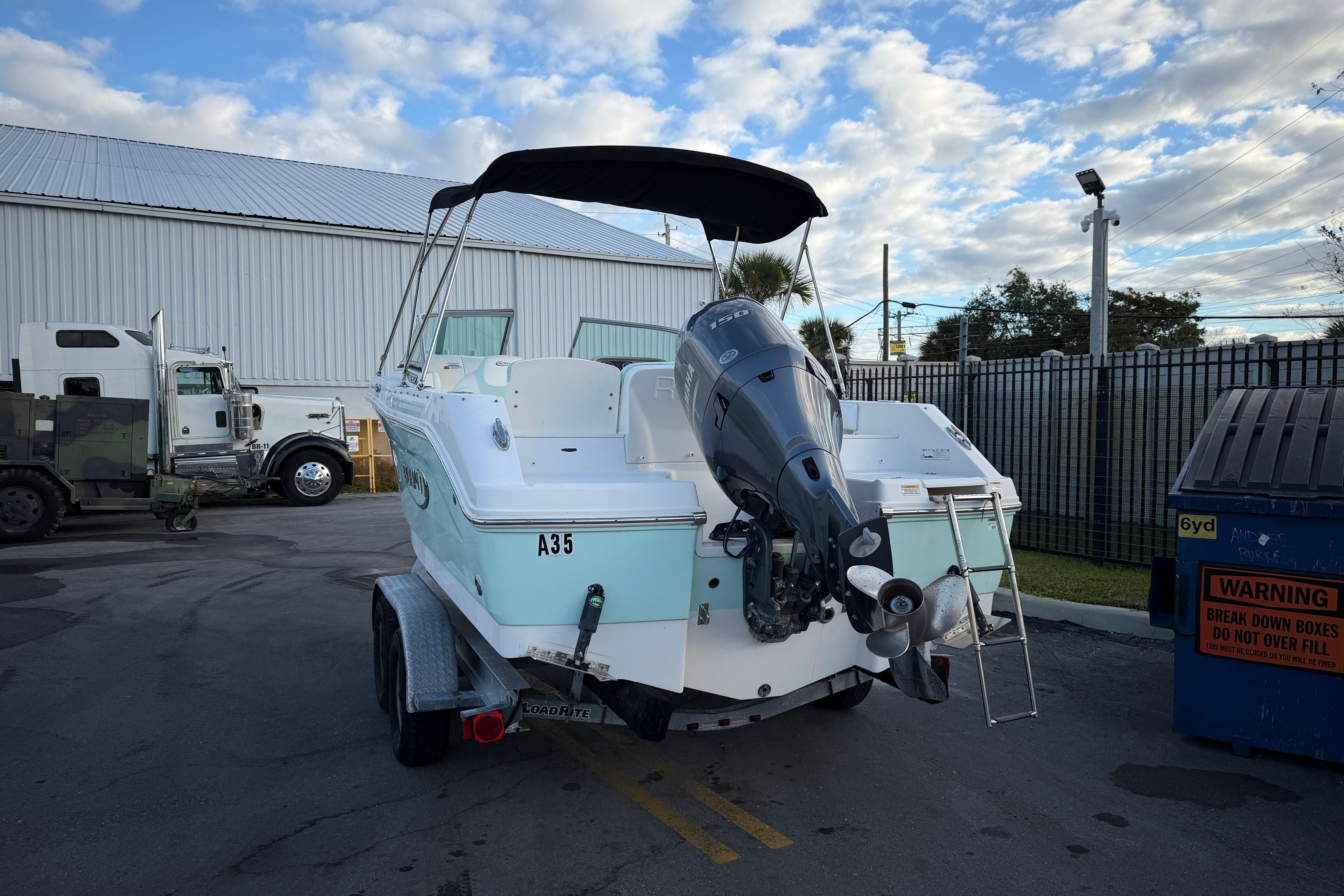 2020 Robalo R207 Dual Console boat on trailer, parked outdoors near industrial buildings.