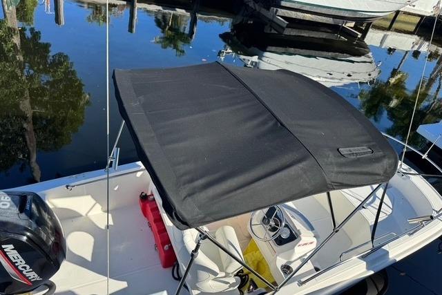2024 Boston Whaler 160 SS boat with black canopy, docked on calm water.