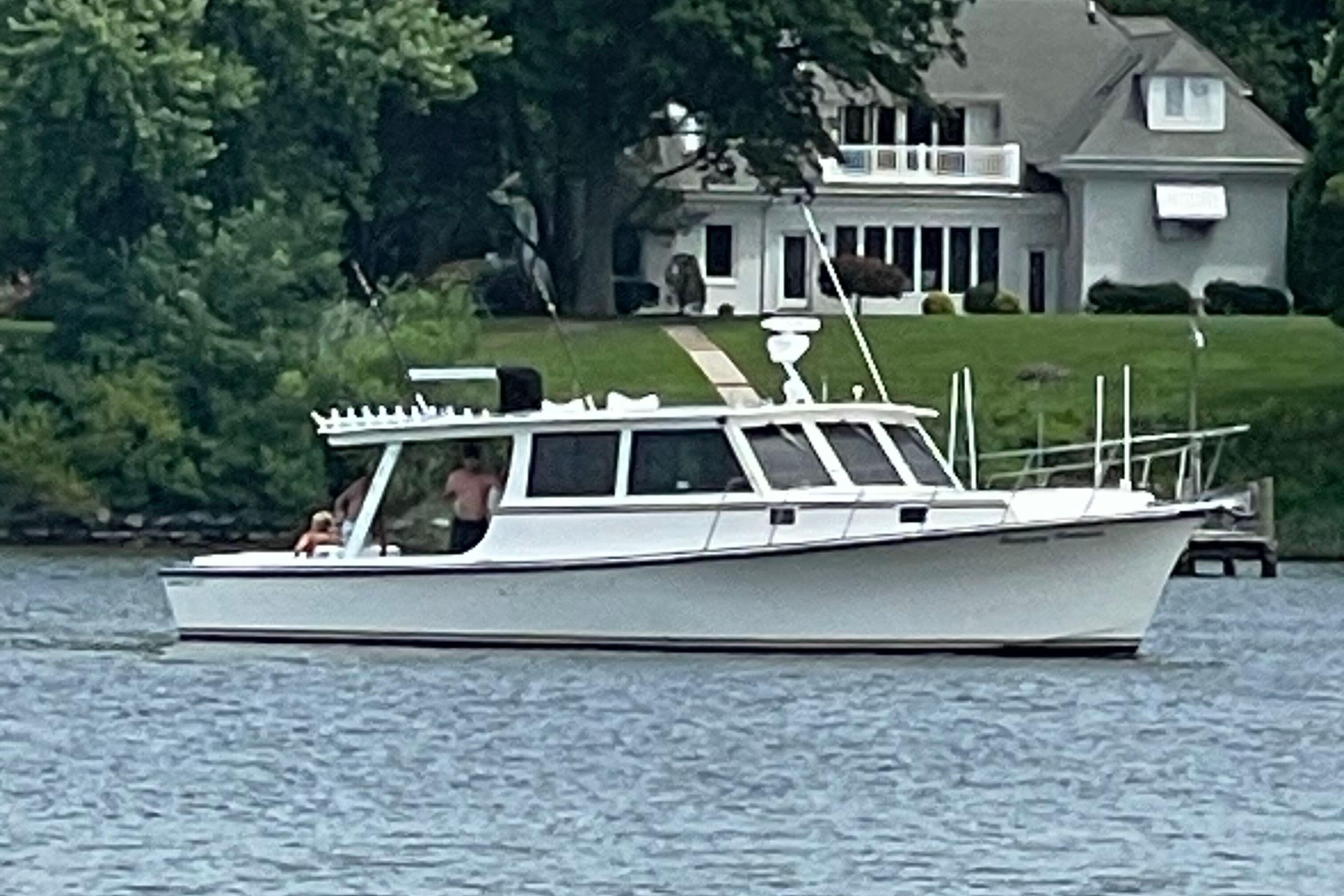 1998 Markley 46 boat on a lake near a house with lush greenery.