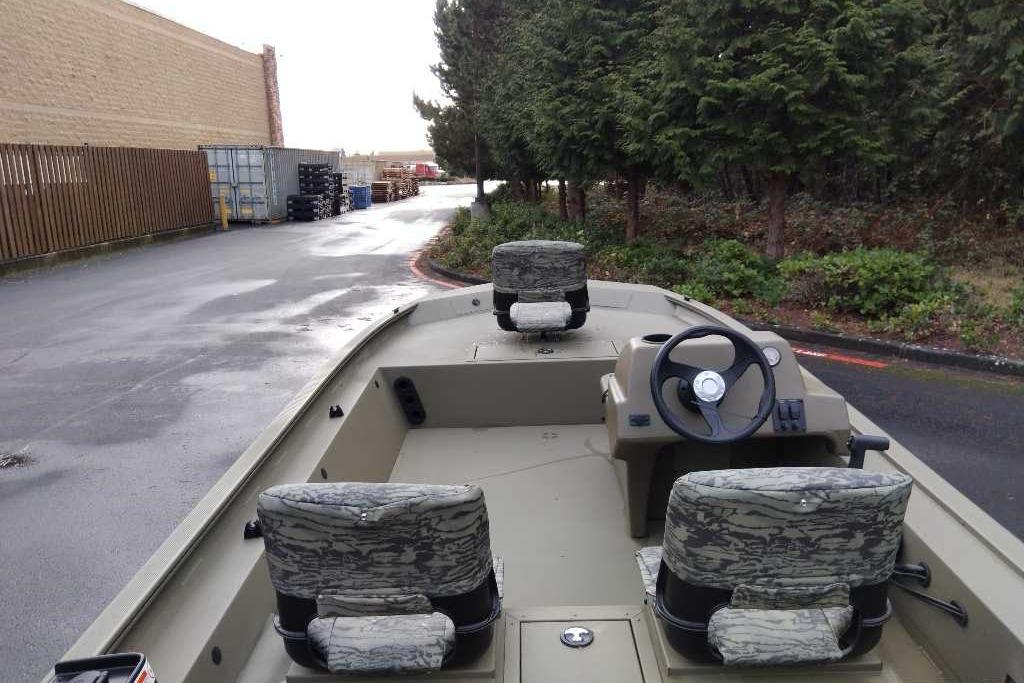 2026 Tracker Grizzly 1754 SC boat with camo seats, parked near trees and industrial area.