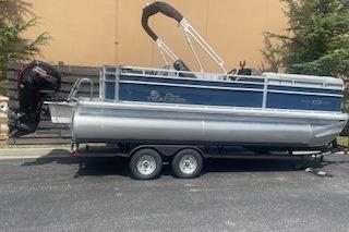 2026 Sun Tracker SportFish 20 DLX pontoon boat on trailer, parked outdoors.