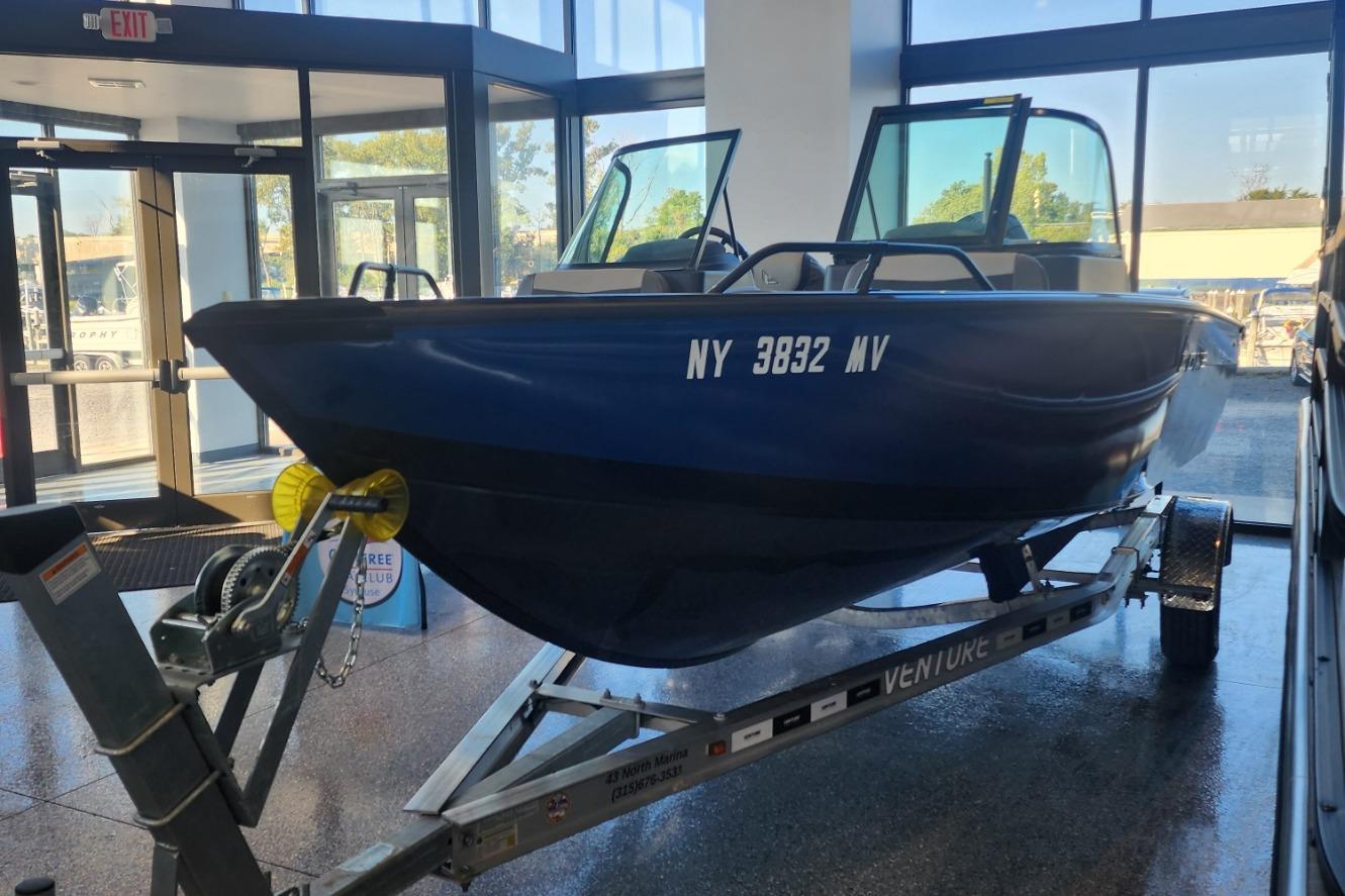Blue Lowe boat on trailer inside showroom, 2023 model, with large windows in background.