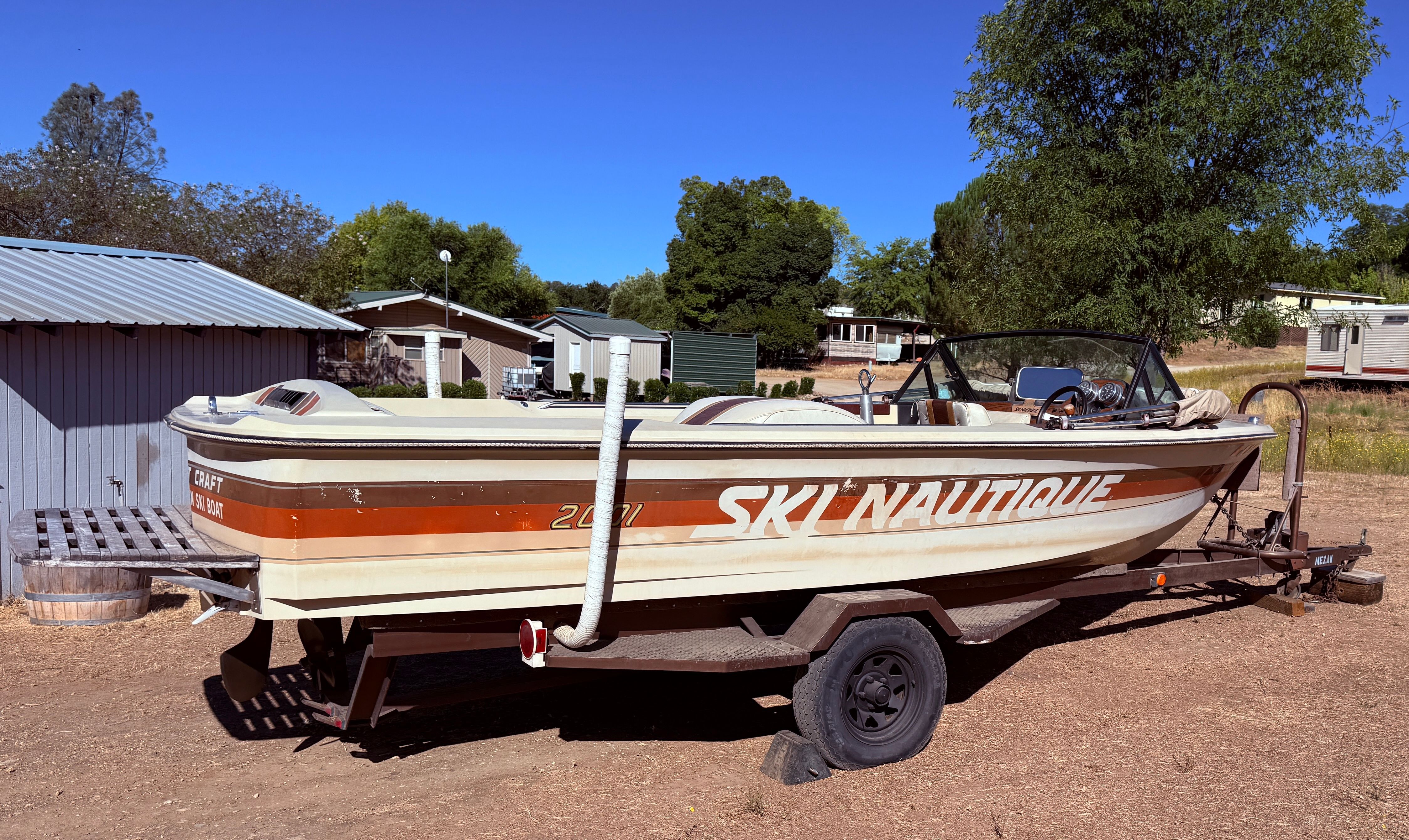 A 1983 Custom Ski Natique 2001 boat on a trailer in a rural area.