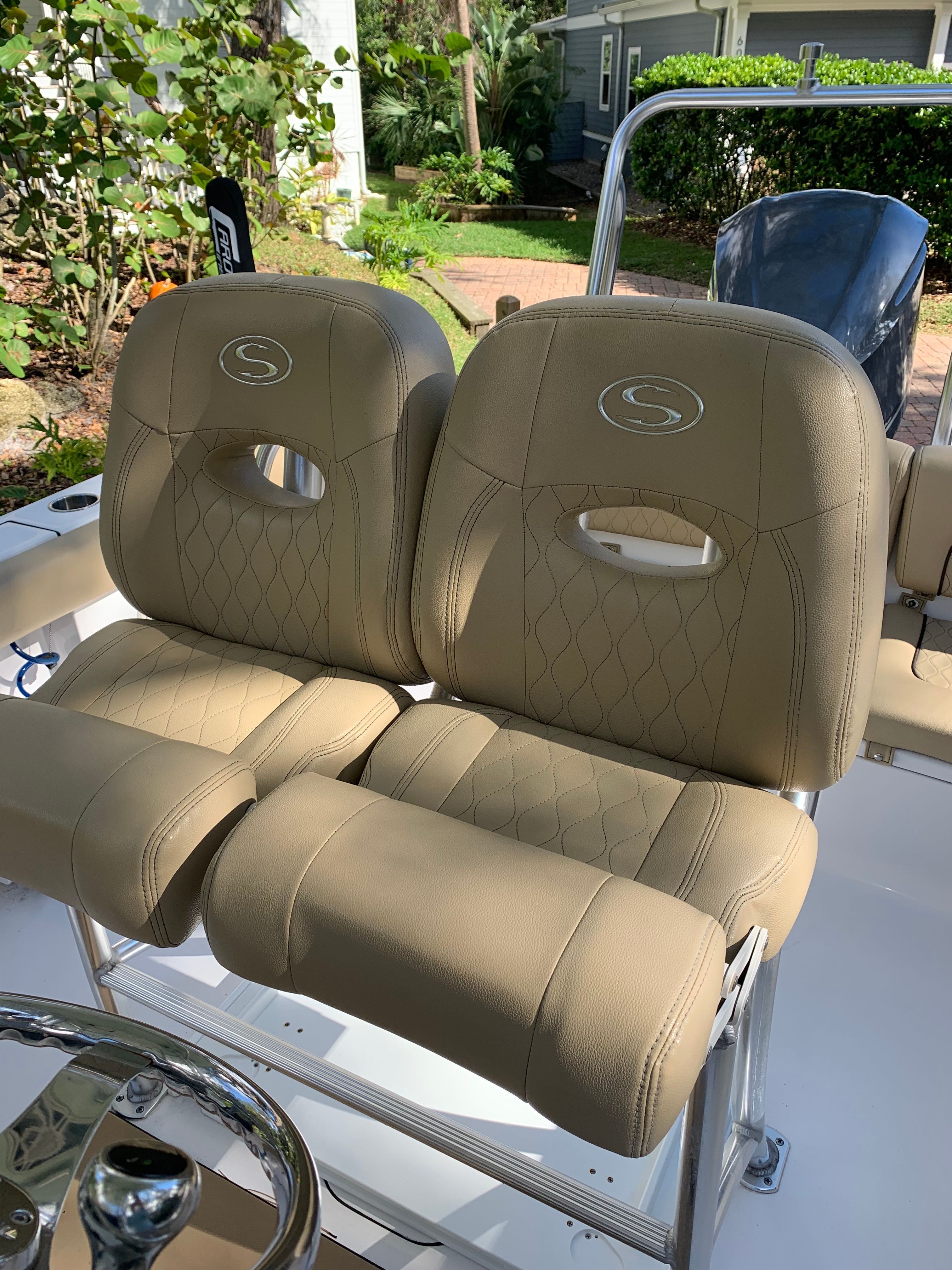 Two beige upholstered seats with Sportsman logo on a boat, surrounded by green vegetation.
