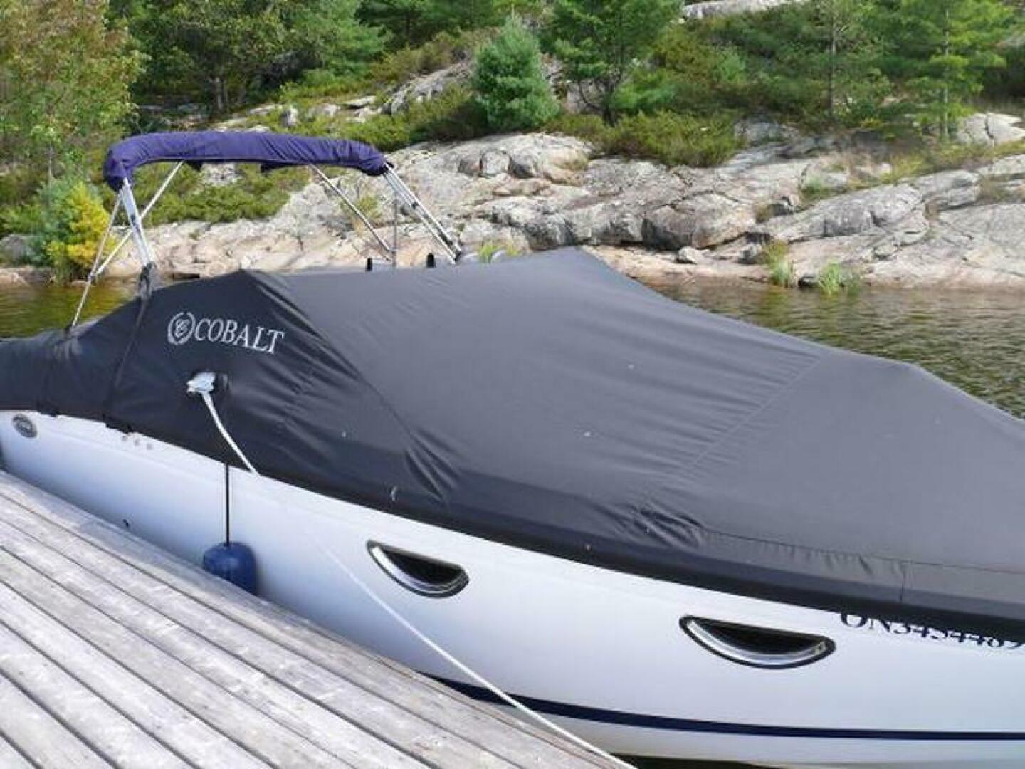 2012 Cobalt 273 boat covered at dock, surrounded by rocky shoreline and greenery.
