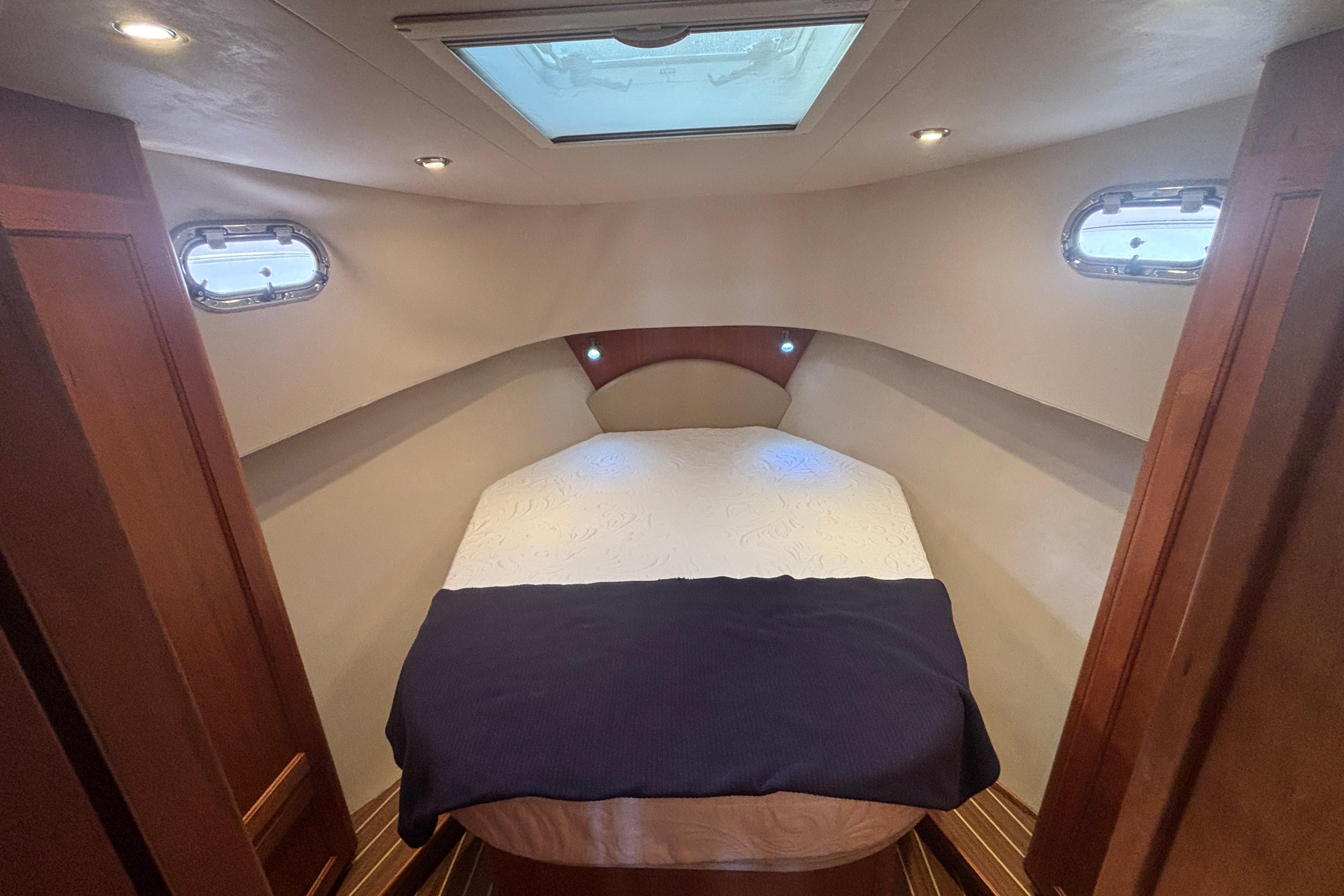 2007 Mainship 34 Trawler cabin with cozy bed, skylight, and porthole windows.