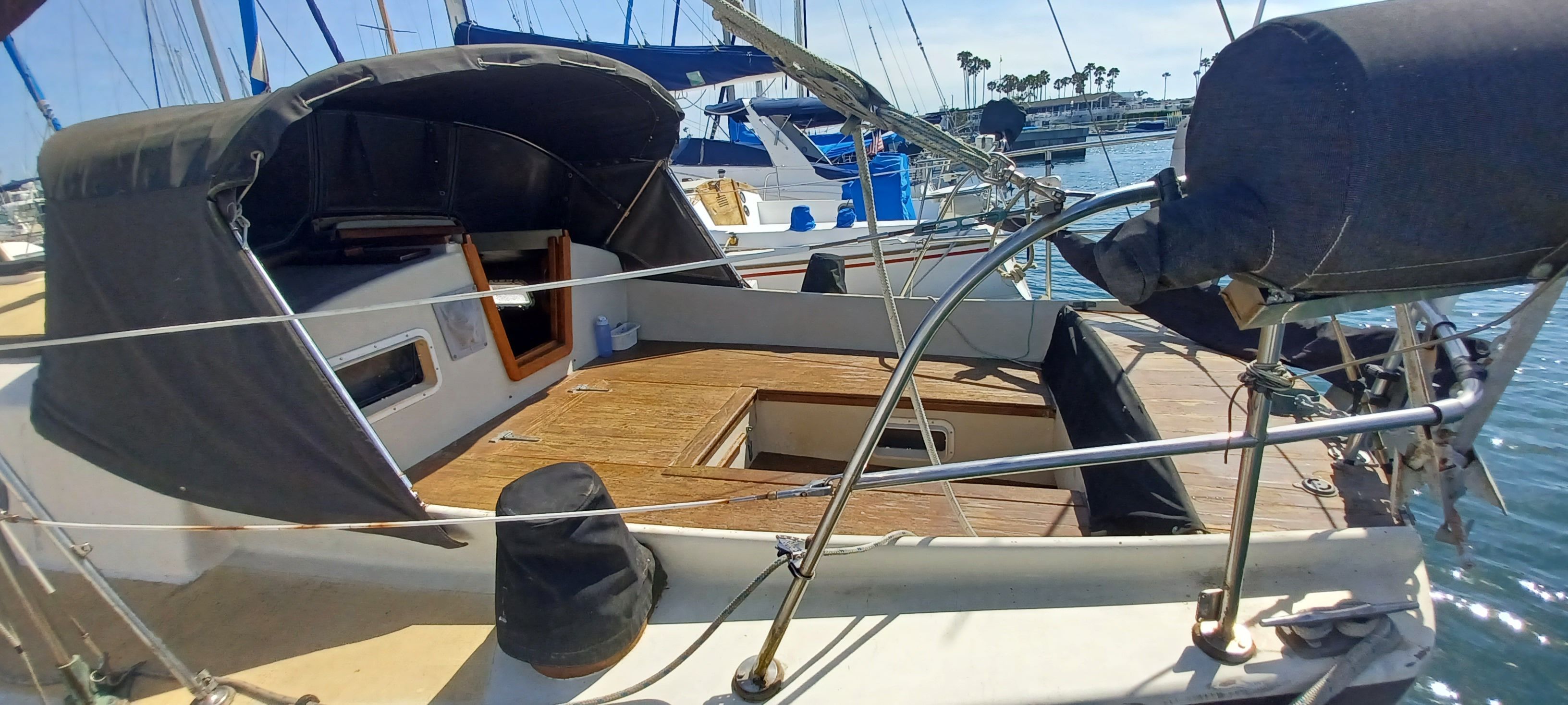 A sailboat with a wooden deck and black canopy docked in a marina.