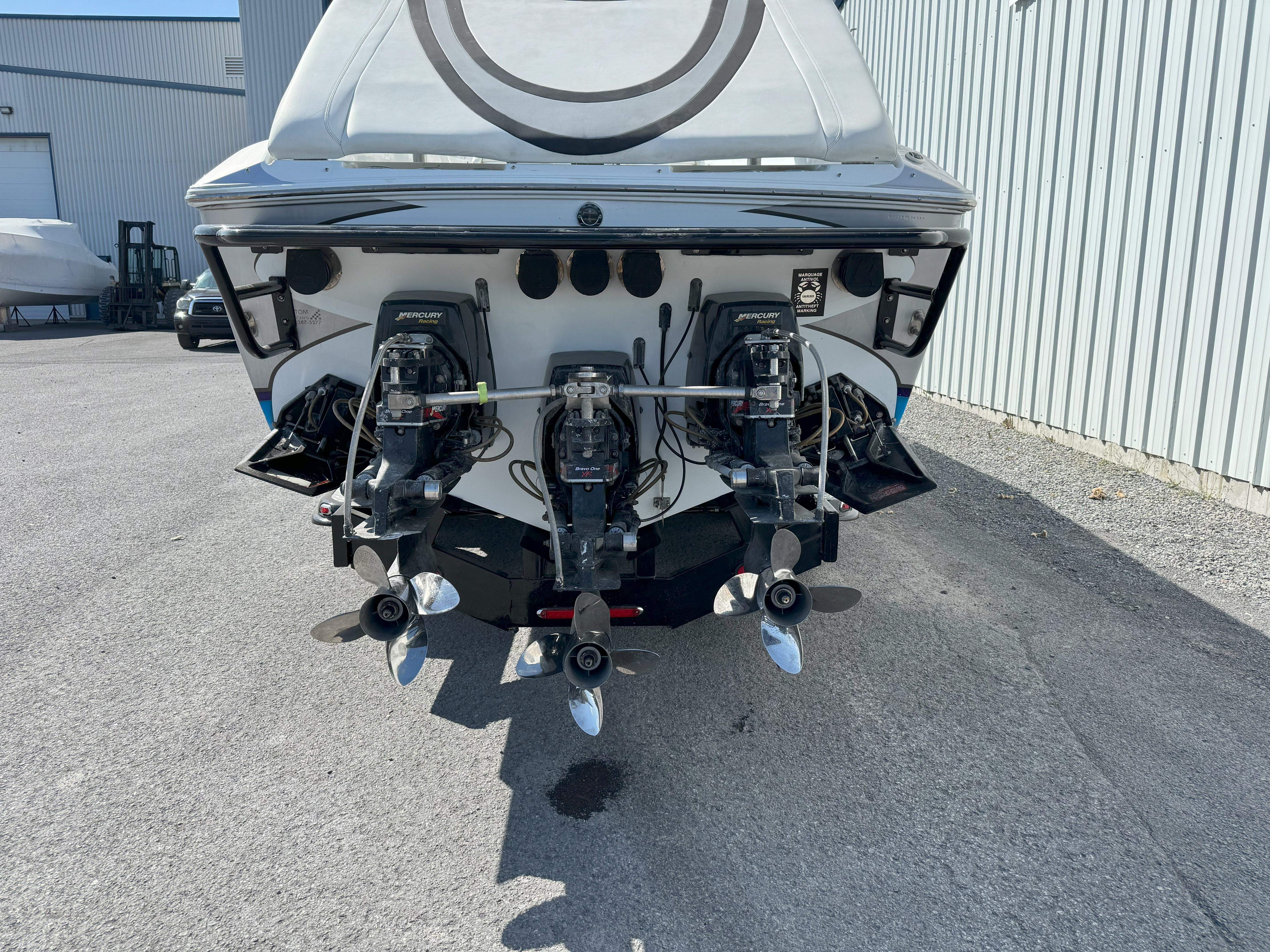 2004 Baja 40 Outlaw boat with triple outboard engines, parked near a metal building.